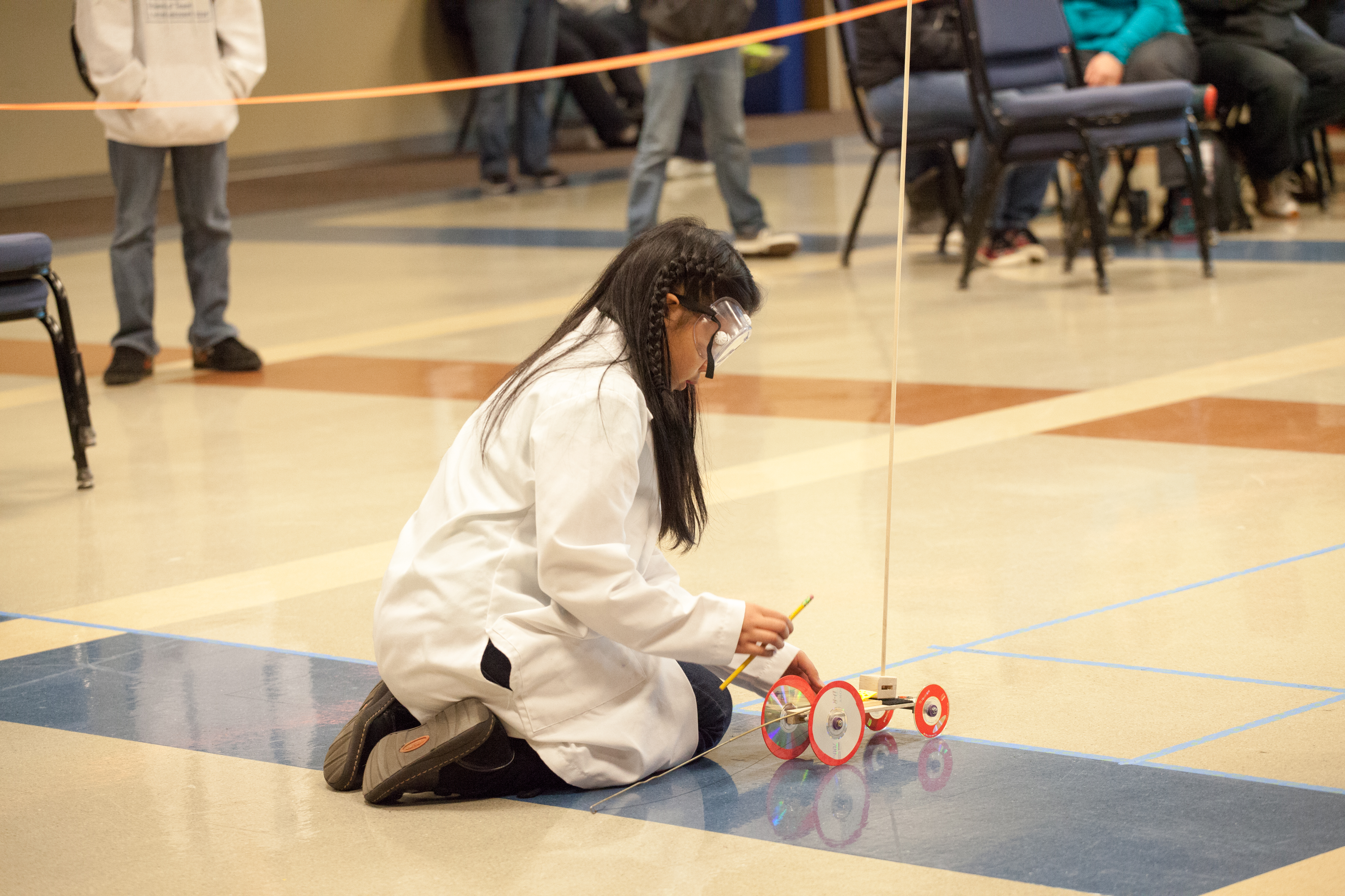 Young woman in white lab coat crouched down with small robotic vehicle.