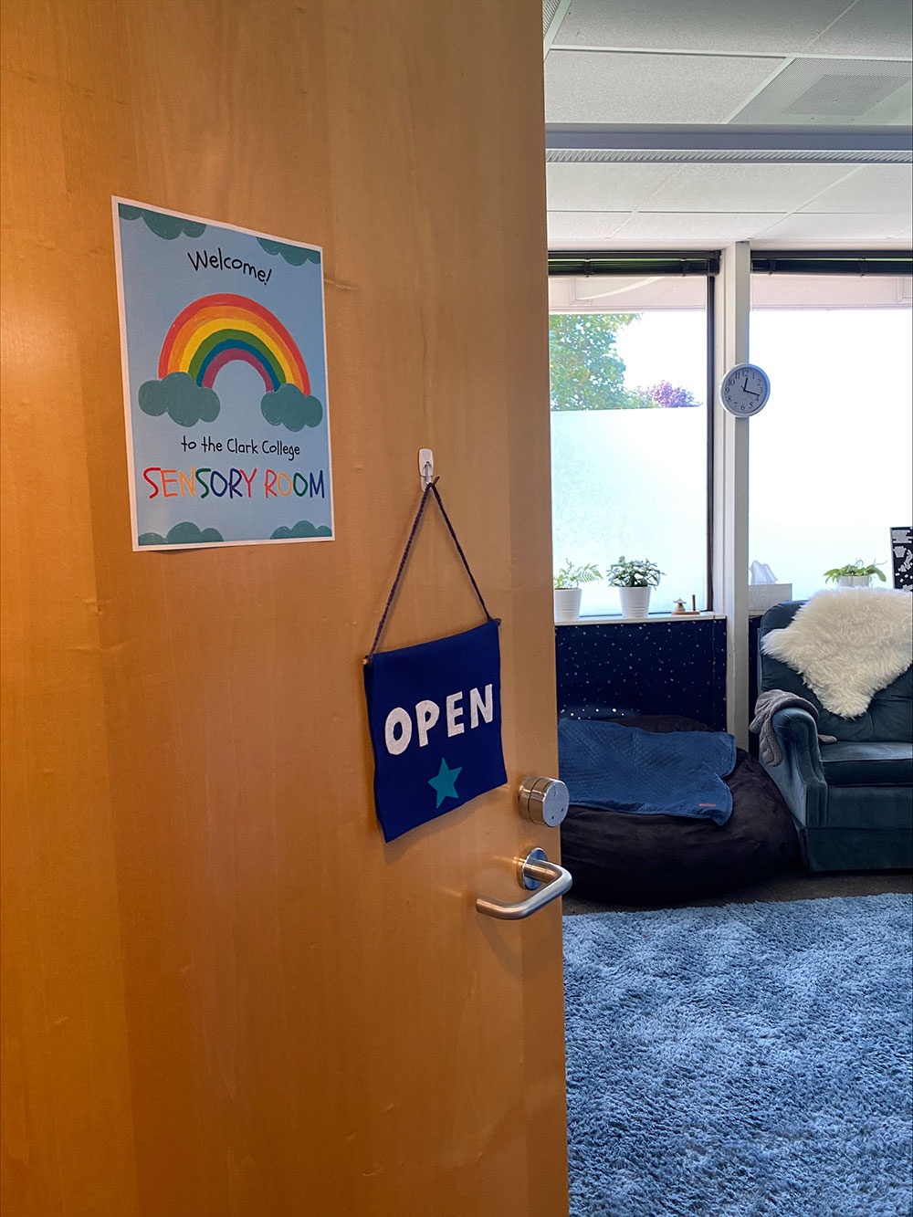 A door adorned with a colorful welcome sign, opening to reveal the interior of the Clark College sensory room.