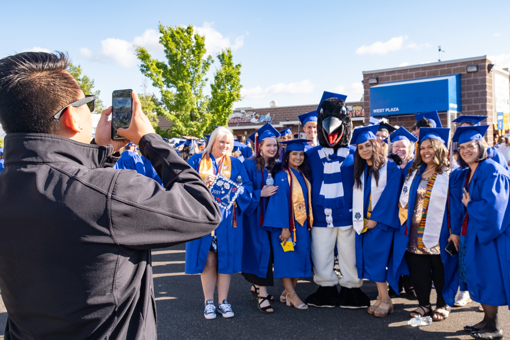 Oswald with a lot of graduates smiling at a man taking their photograph with a phone.