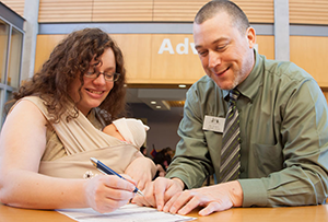 woman with infant being helped by a college employee