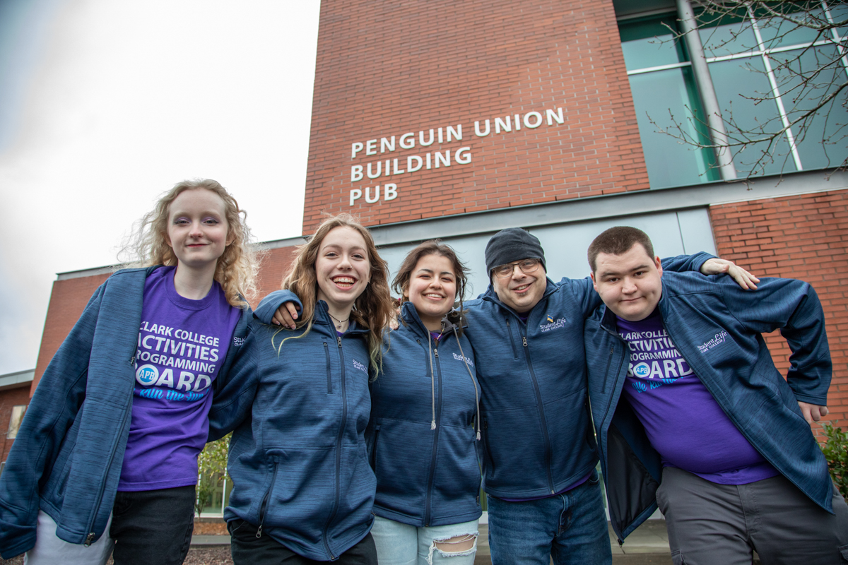Three students smiling at camera with campus in background