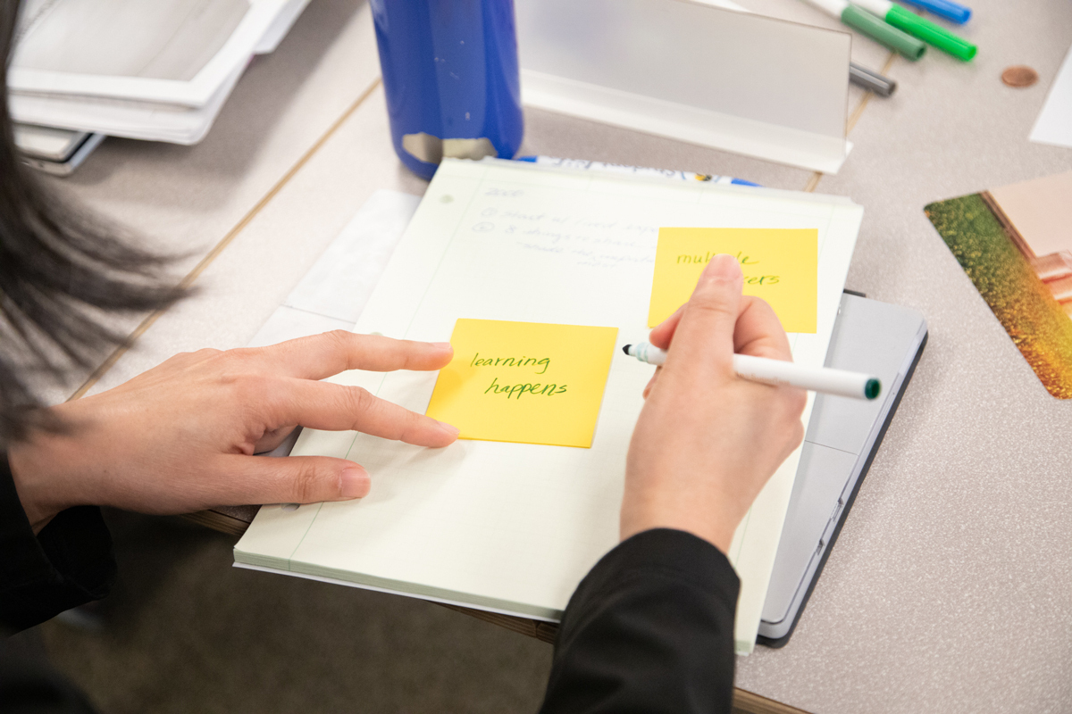 image of woman writing on reminders on sticky notes. One says, 'Learning Happens'.