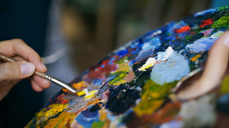 close up woman's hand mixing paints with brush on a palette