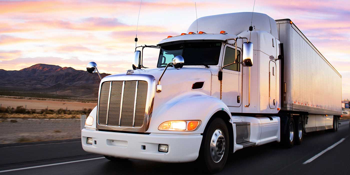 A truck driving on a highway with mountains in the background and a colorful sunset sky.