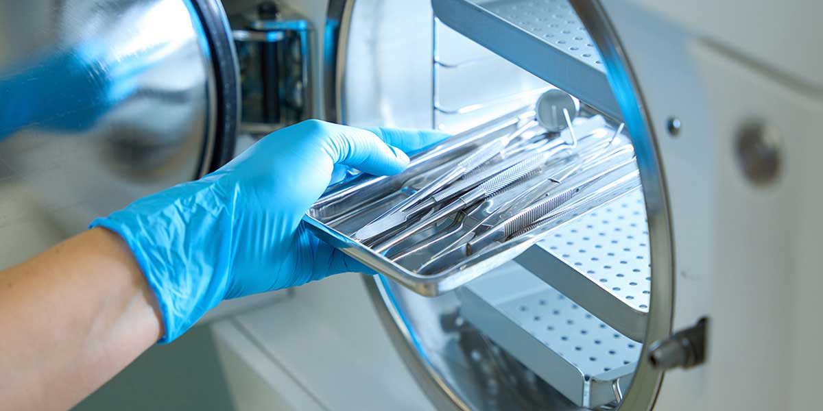 A gloved hand placing medical instruments into a sterilization machine.