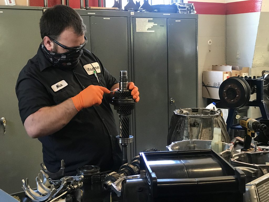 Student Nick Ferguson, wearing a PPE mask and gloves, works on an automotive gear.