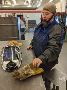Welding student Jessica Pellham in welding gear, about to put on heavy welding gloves