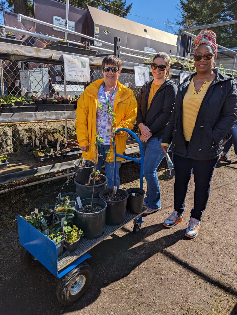 Three people stand beside a cart of plants.