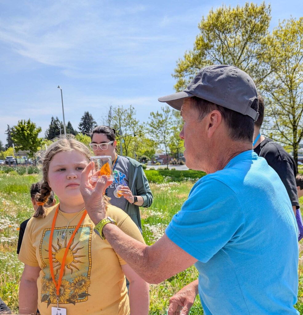 Steven Clark (Biology) shows future penguin Megan a pollinator her captured in the STEM bee garden. Megan's mother Rachel works in WES.