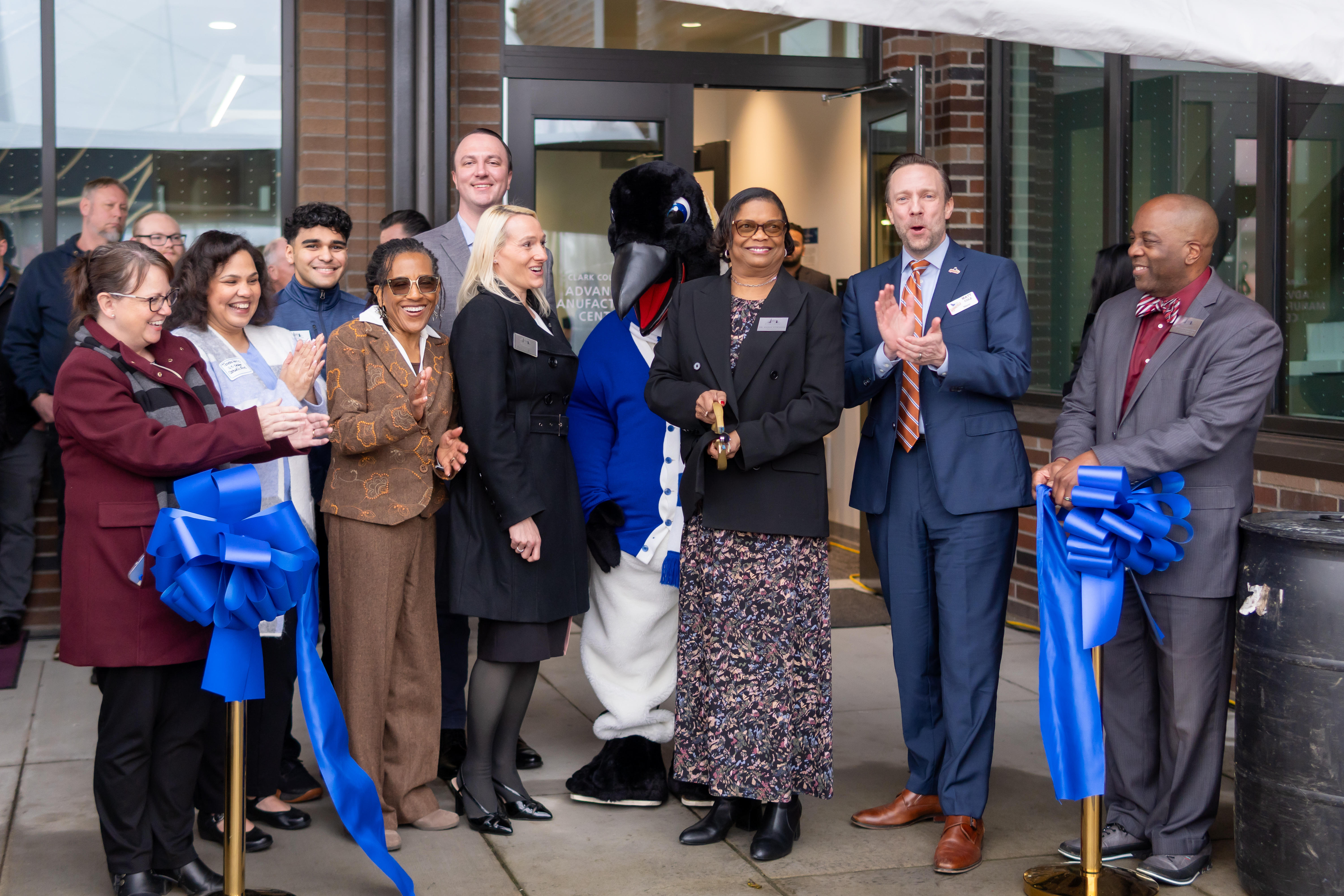 Dr. Edwards stands with group of partners, including administrators, trustees, and legislative representatives, as she cuts a blue ribbon with giant gold scissors.
