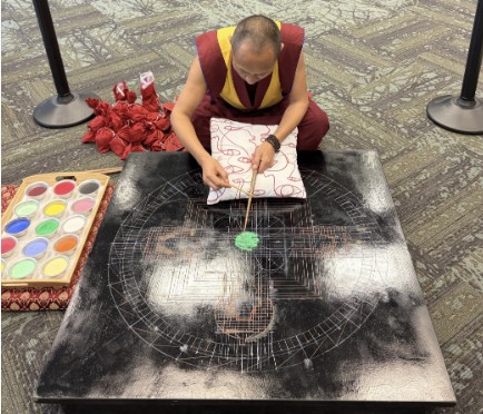 A monk leaning over a black block that contains only one small pile of green sand