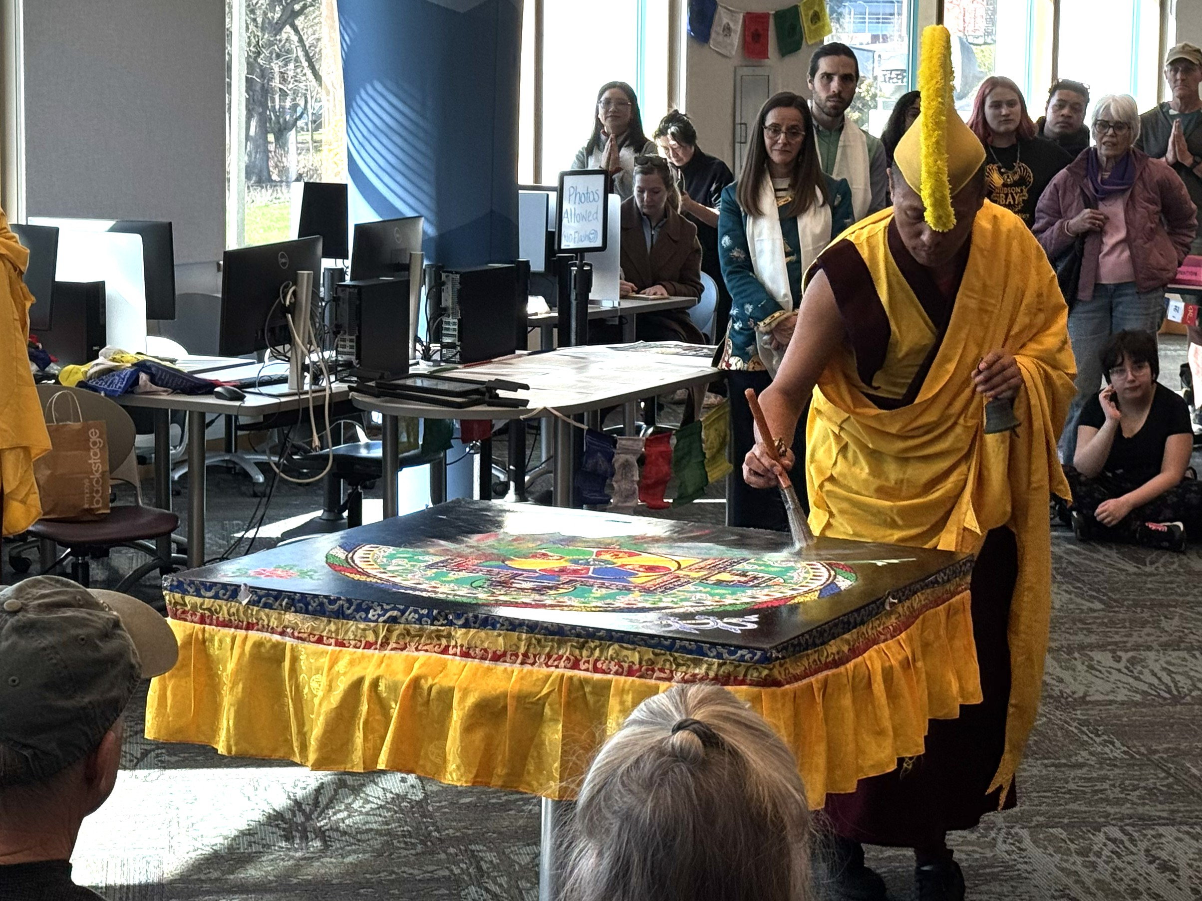Monk using a paint brush to sweep sand from mandala into a pile