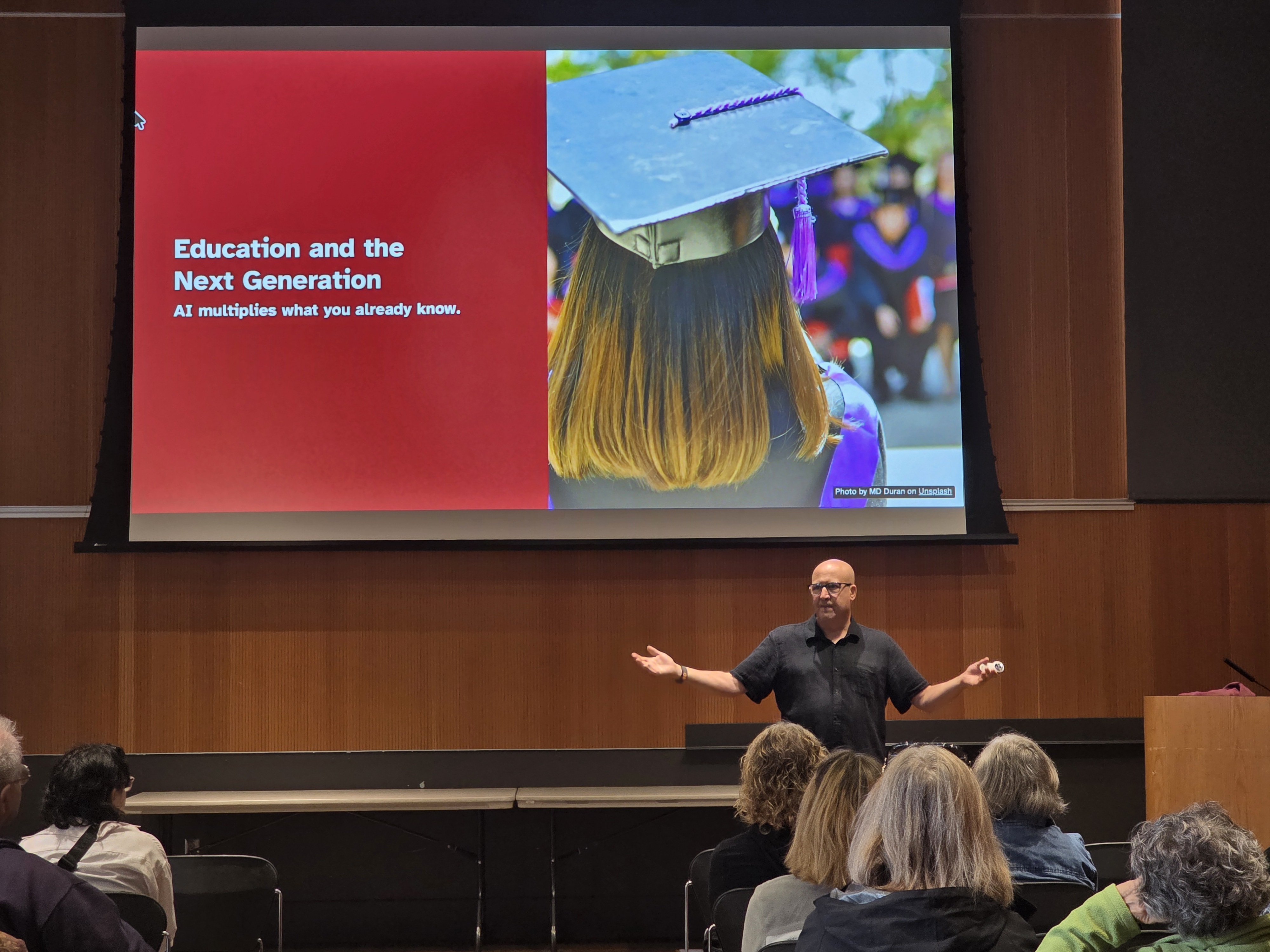 Bruce Elgort in front of presentation about AI in education, speaking to a seated audience