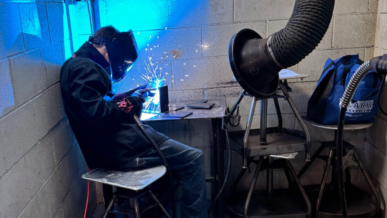 Student in a welding mask welding material with blue sparks flying up