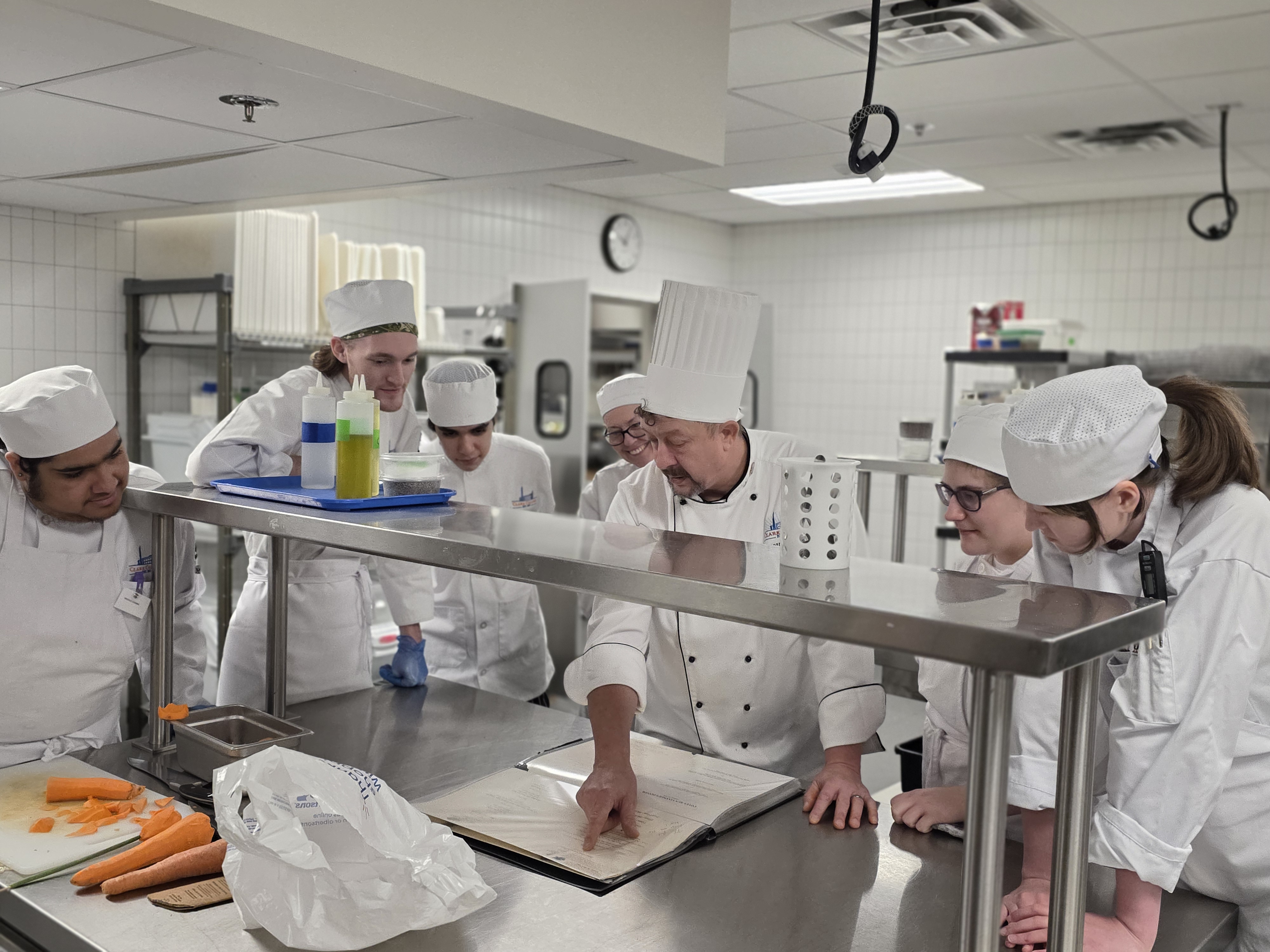 A group of students gathered around Chef Aaron in the kitchen