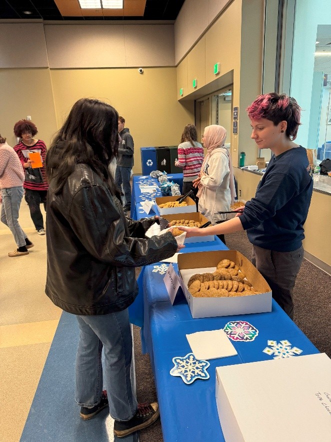 A student behind a table hands a cookie to another student