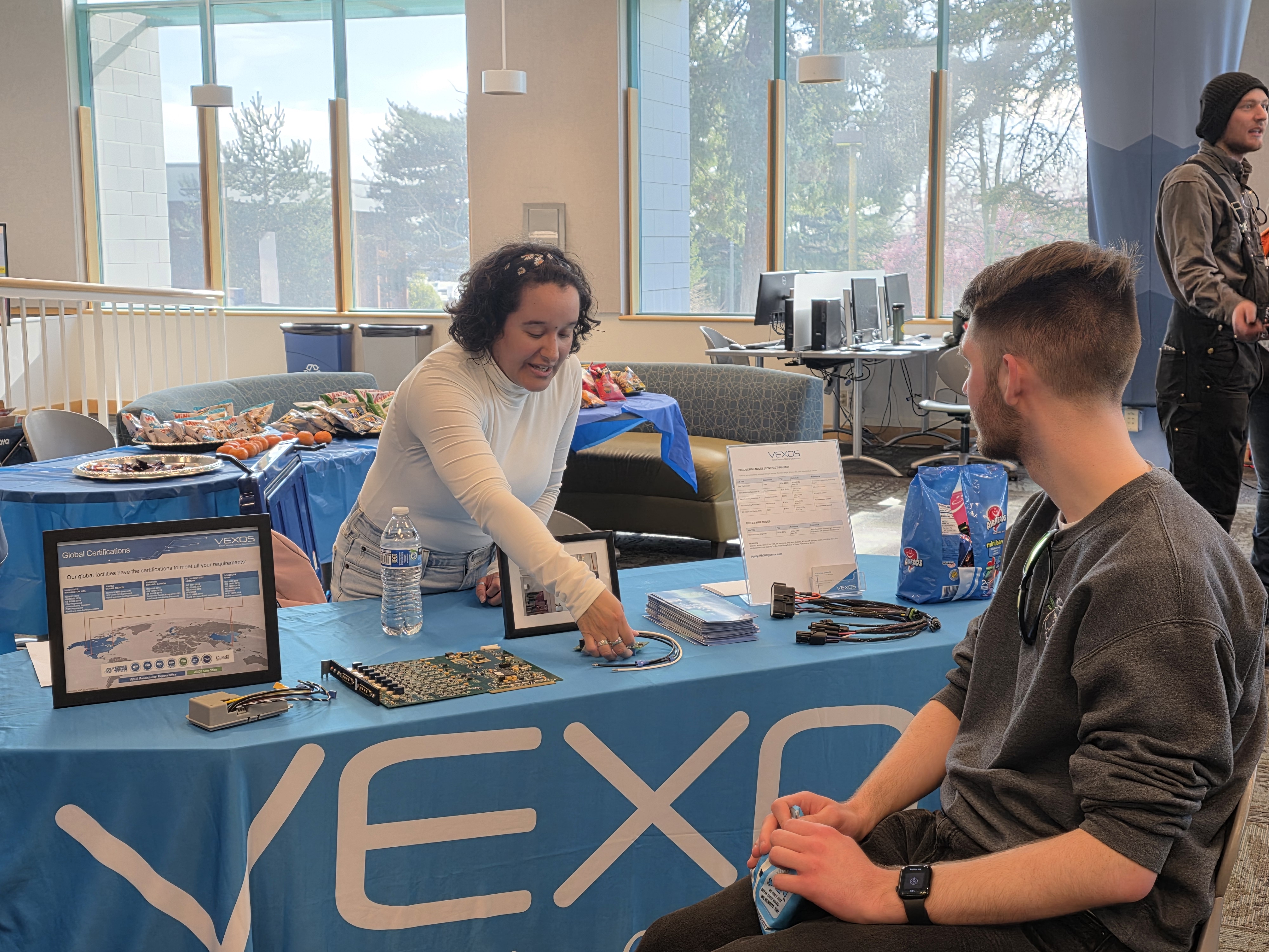 A vendor at the Advanced Manufacturing Career Connect event points to material on her table as a student sits and observes.