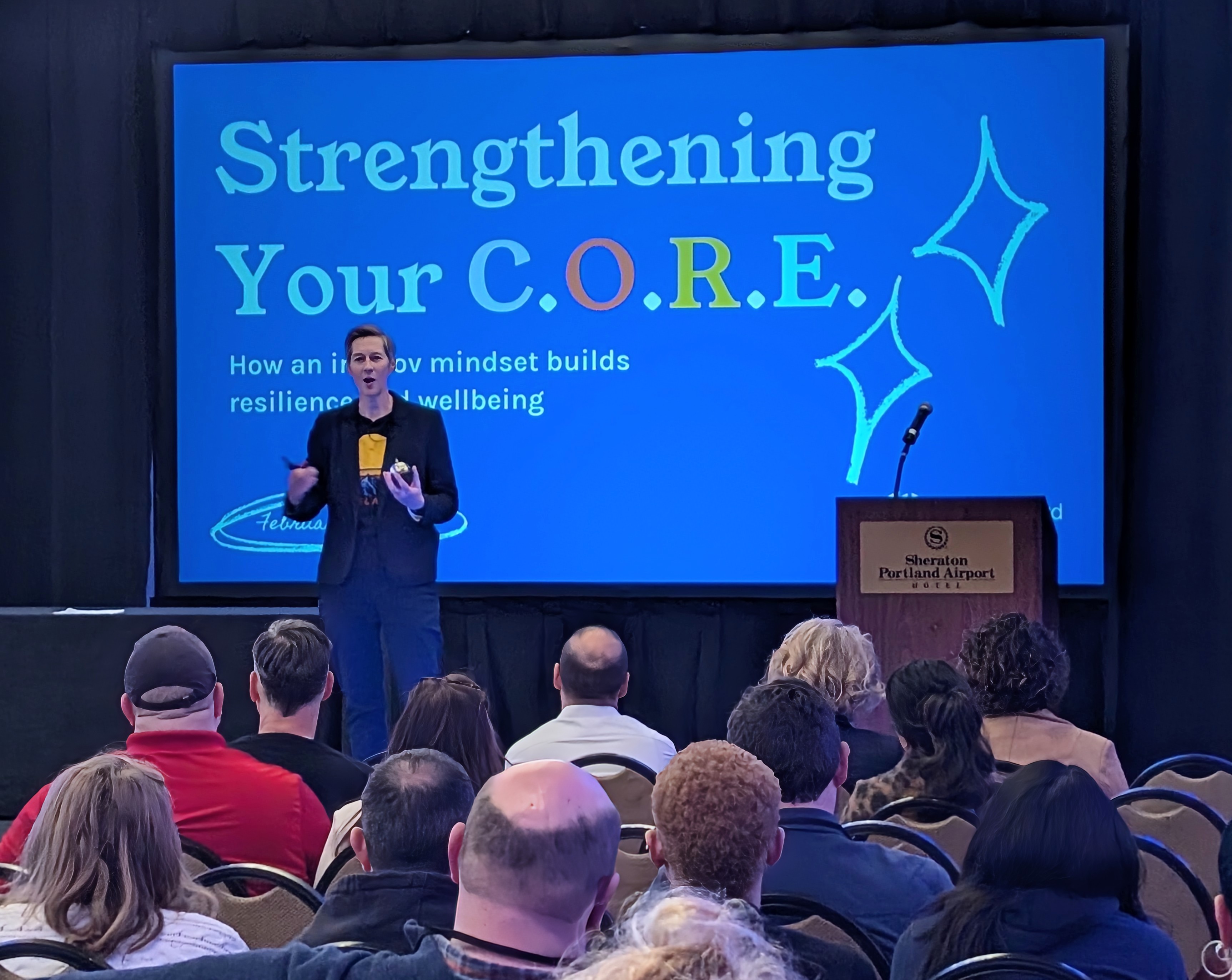 Dr. Sue Orchard stands on a stage in front as she presents at a conference.