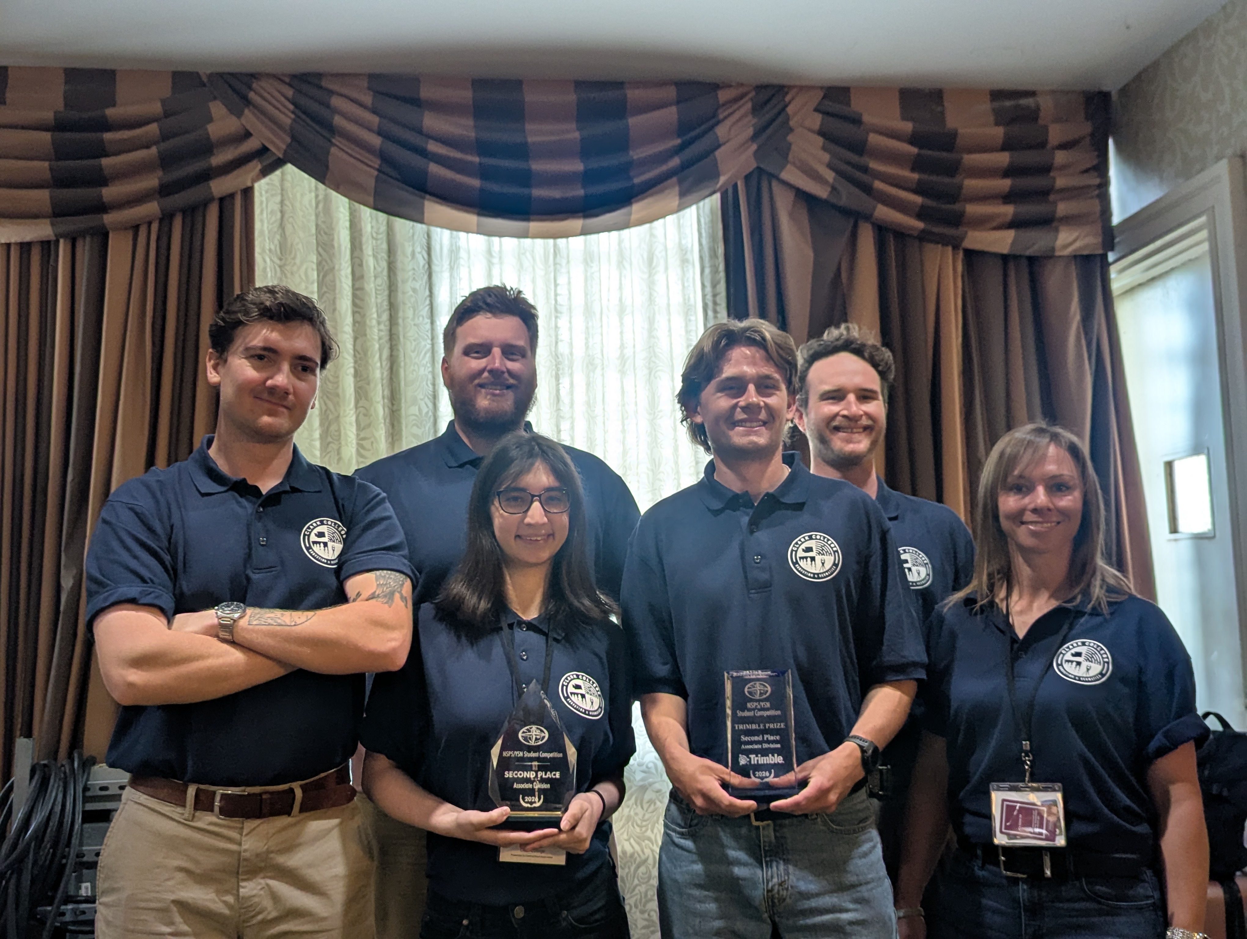 Six survying and geomatics students standing in front of a curtained window, two of whom are holding glass trophies.