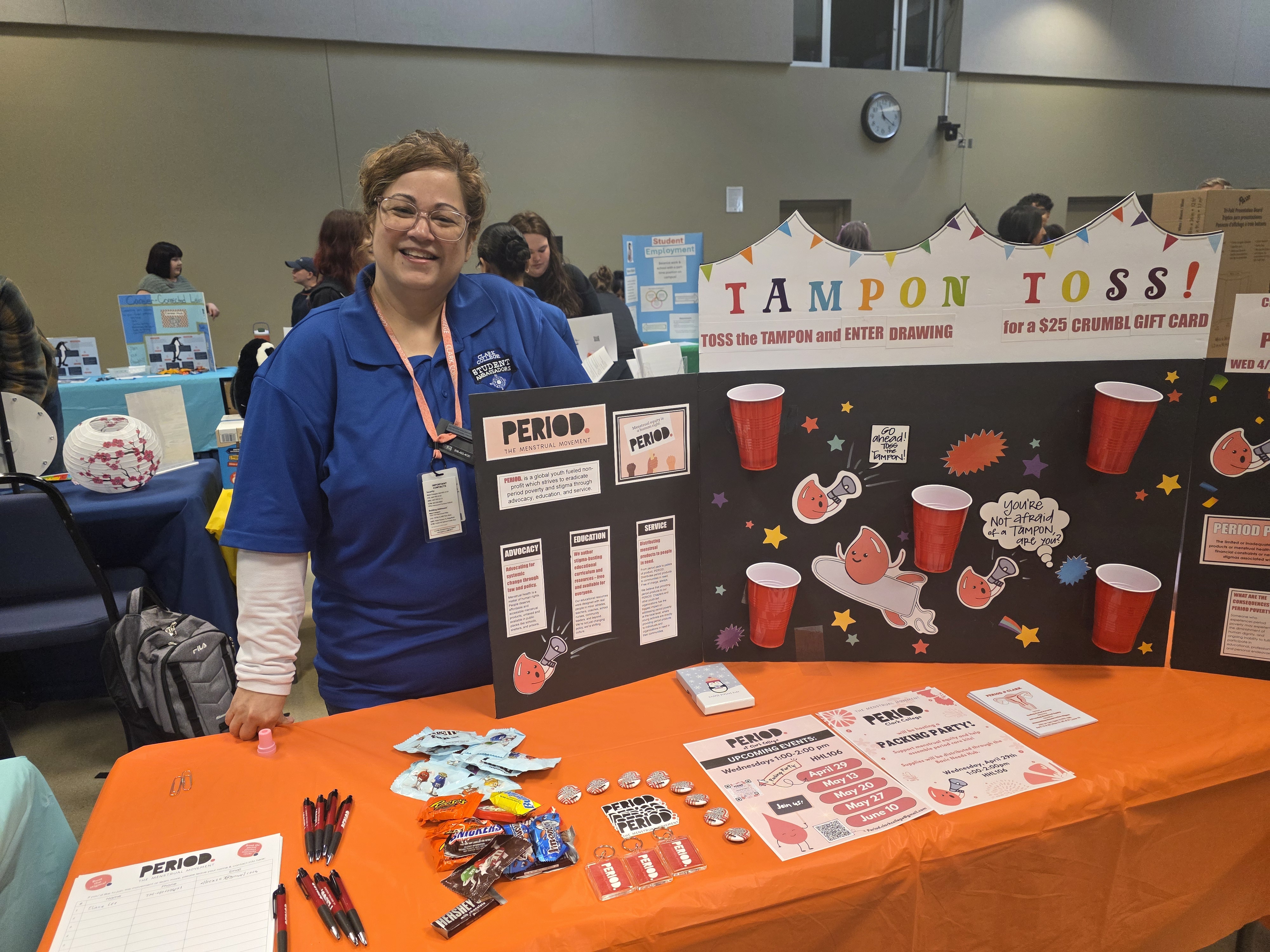 Jude stands behind a table with a poster that says "Tampon Toss"
