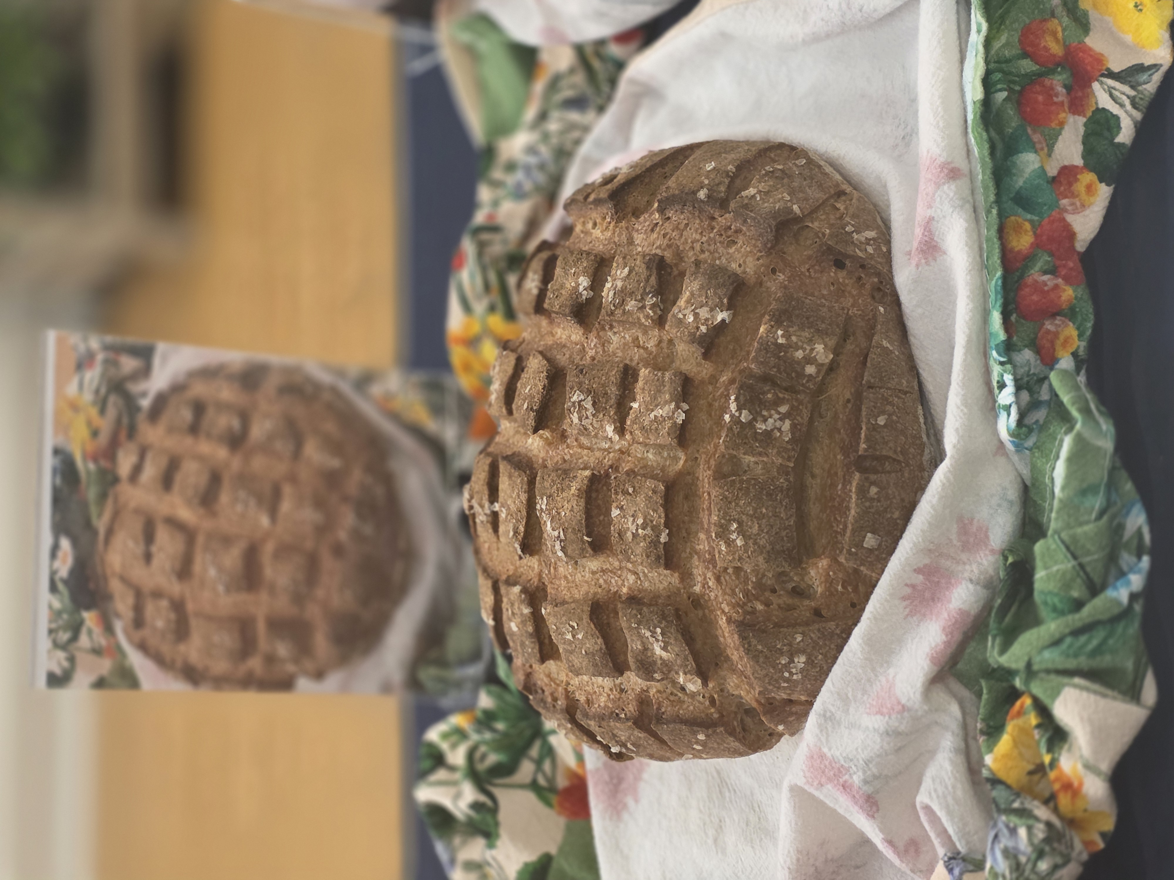 A rustic bread with scoring sits on a colorful plate