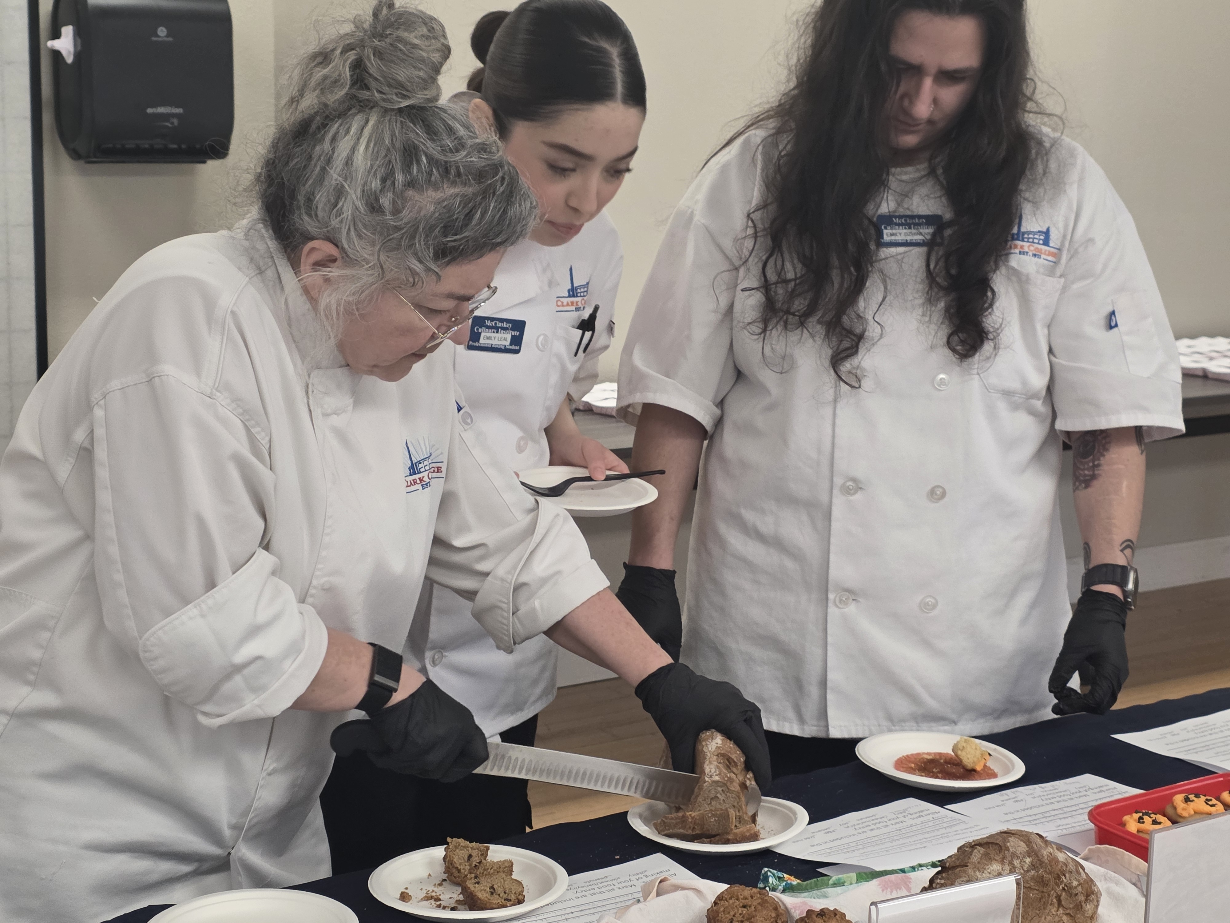 Chef Melanie slices a loaf of bread as students look on
