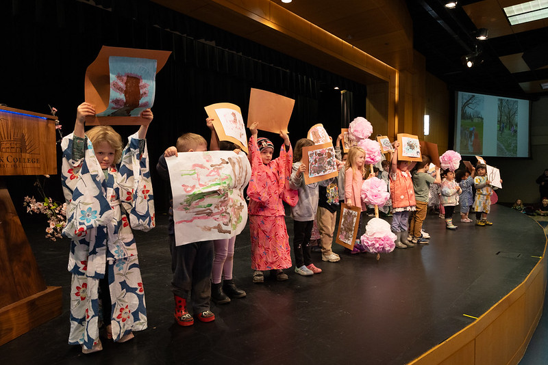 Children dressed in kimonos on stage holding their artwork