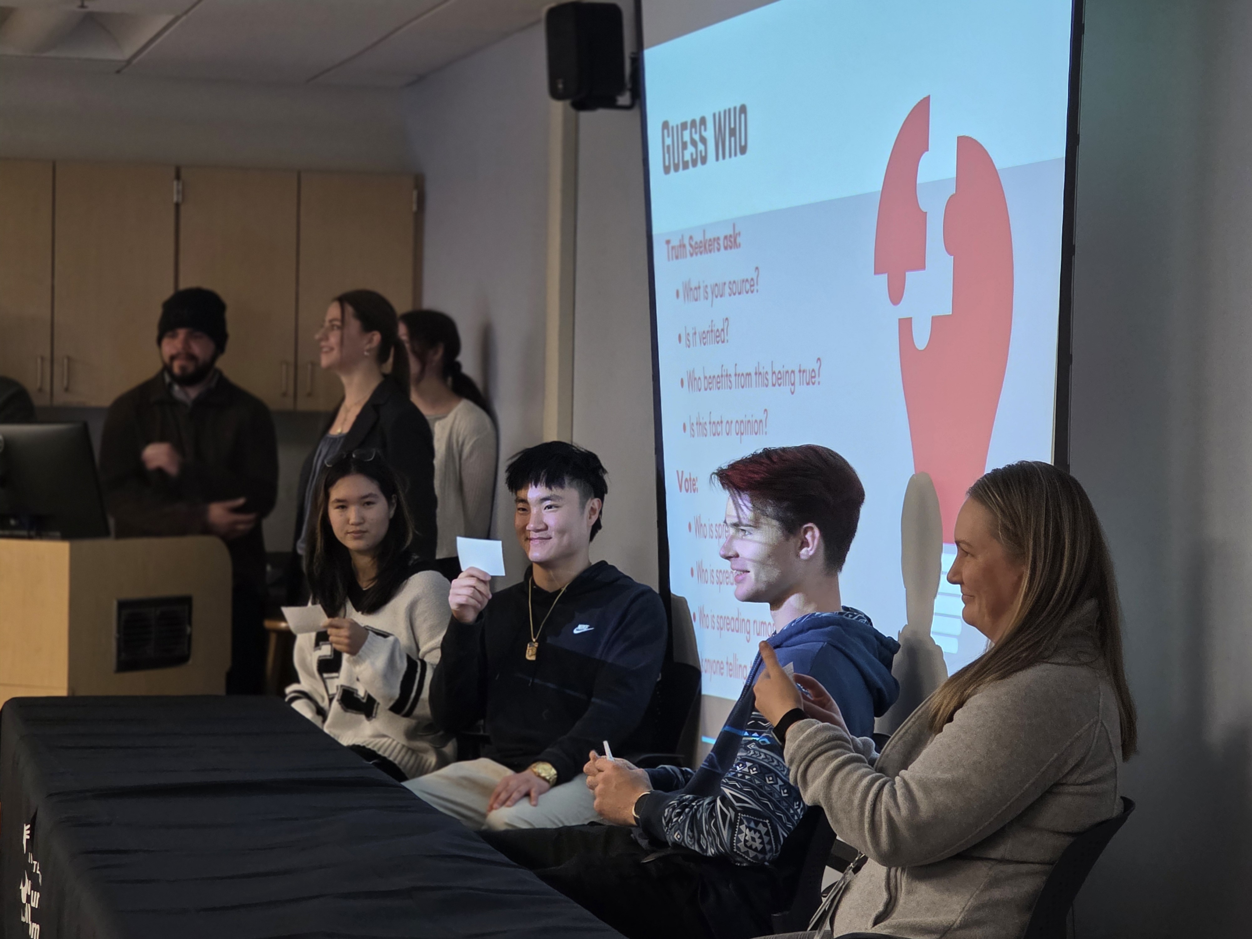 Four students read from notecards at the front of a classroom