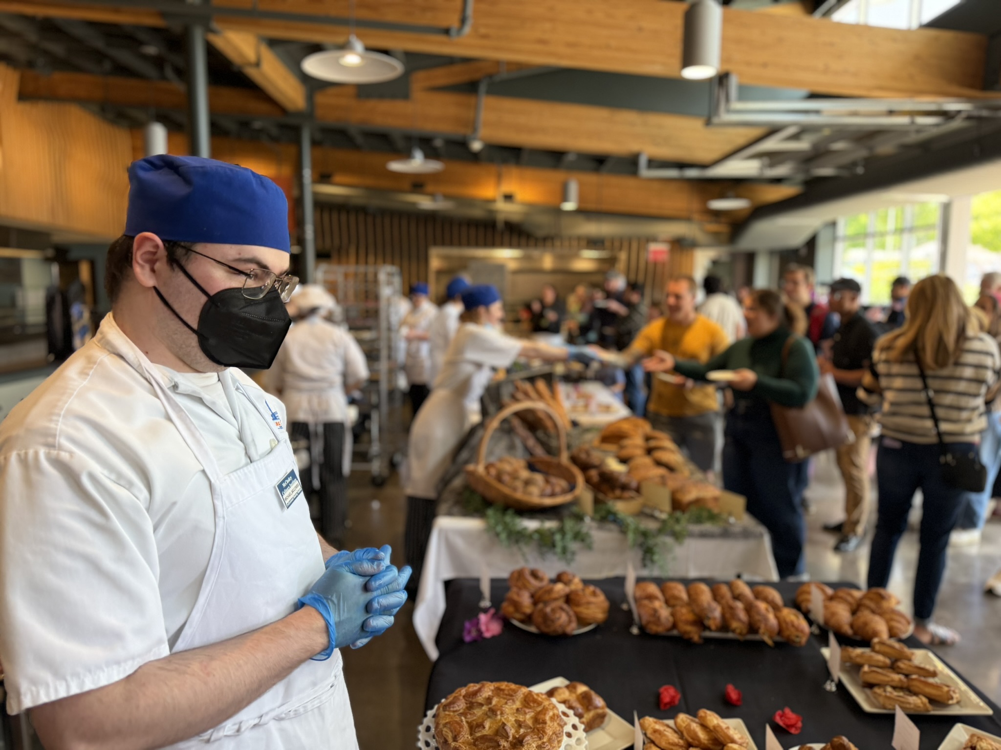 Baking student standing behind a table as guests browse his baked goods