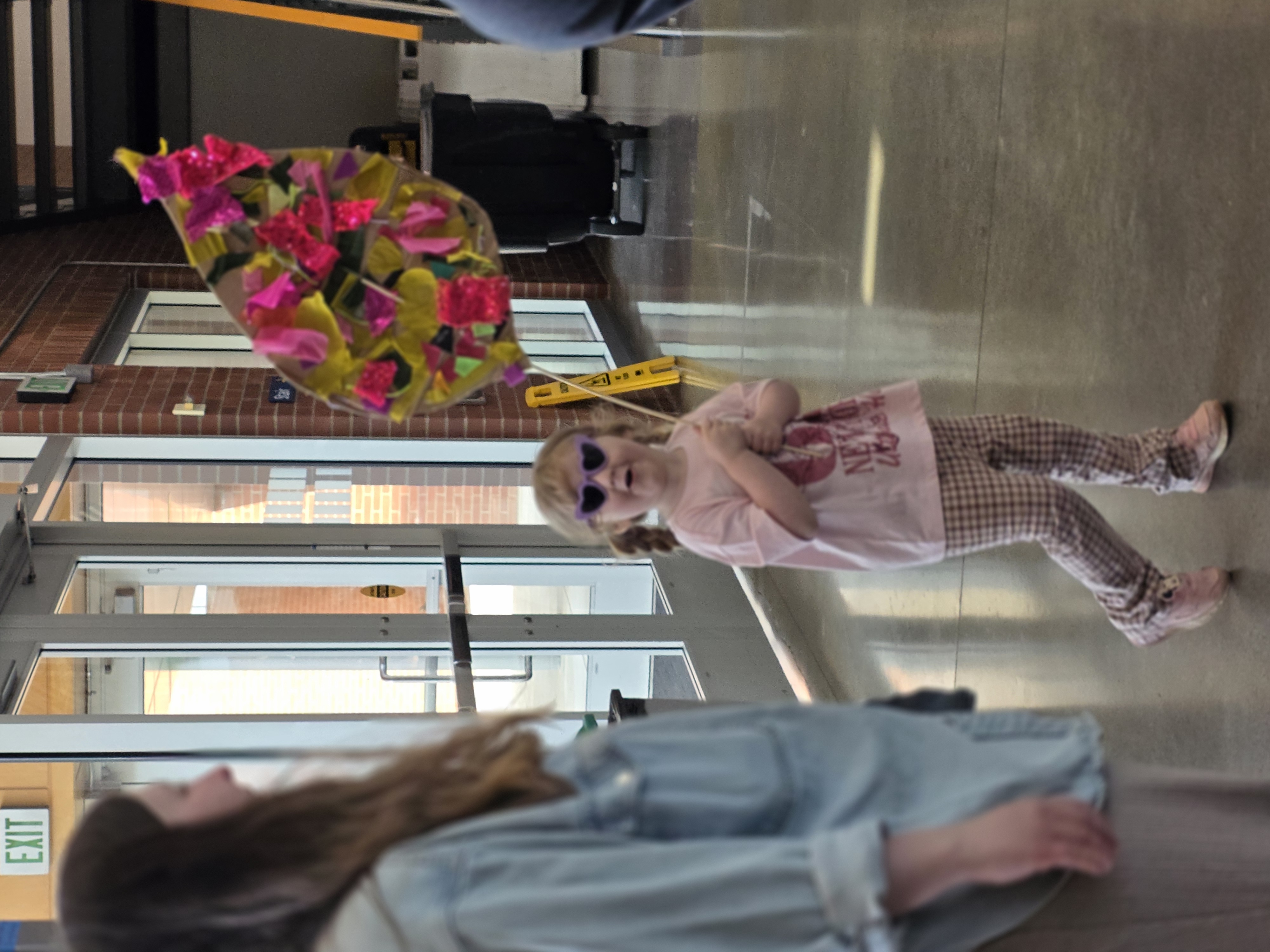 Little girl wearing sunglasses holding a giant homemade pink and yellow leaf
