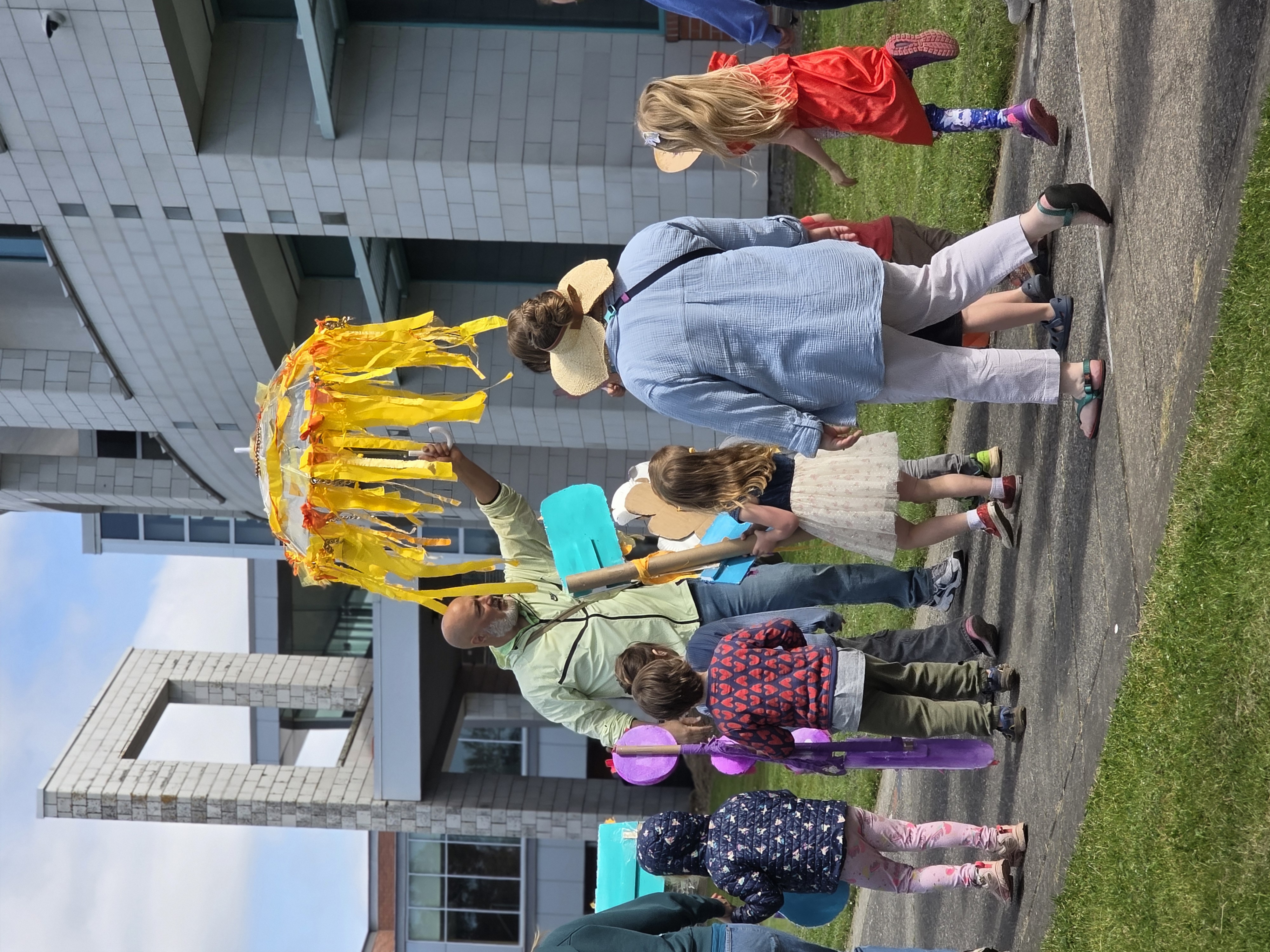 Man holding yellow prop with streamers, leading group of children during parade