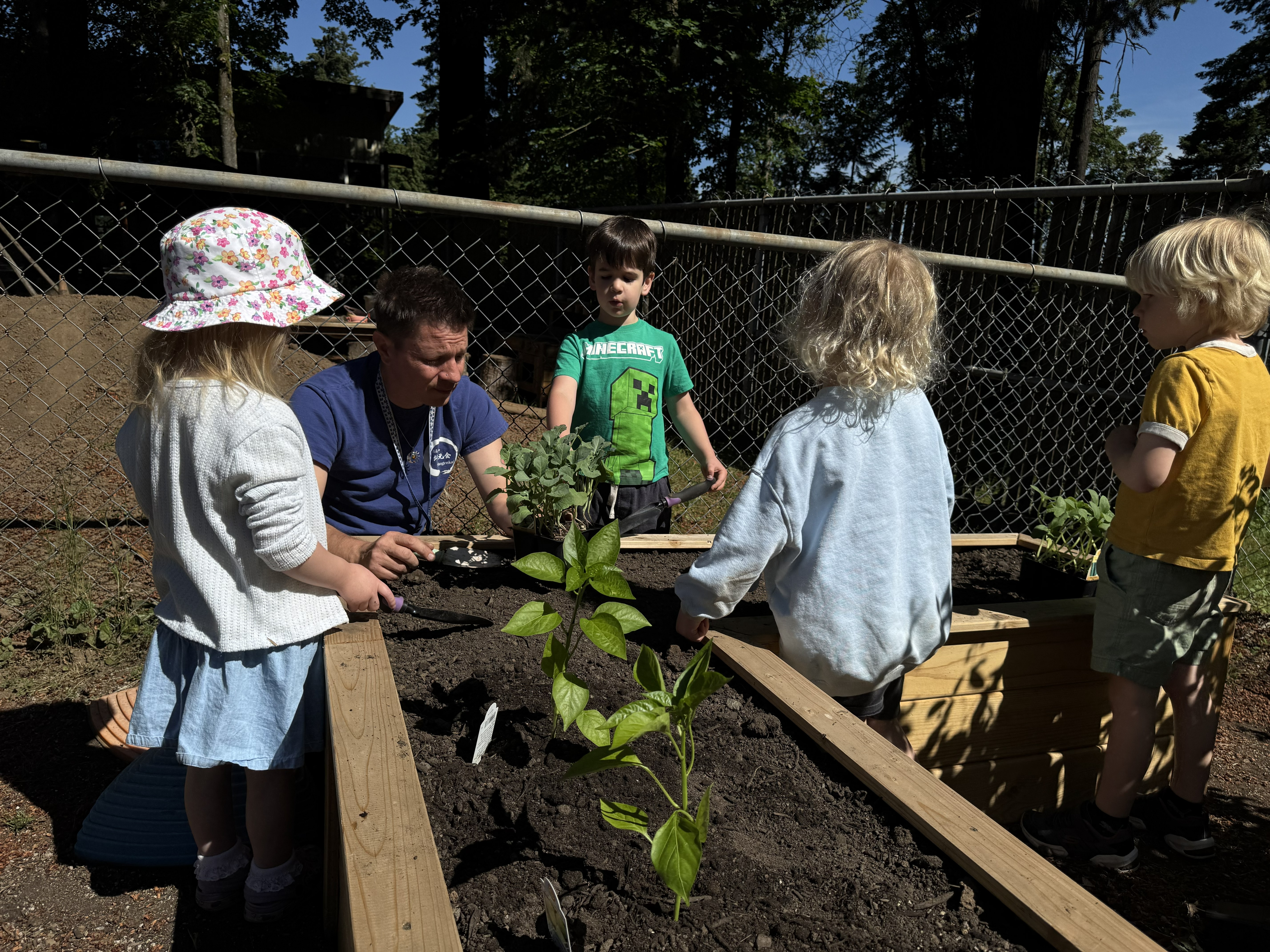 Outdoor teacher Matthew Philbrook and children standing around a planter box