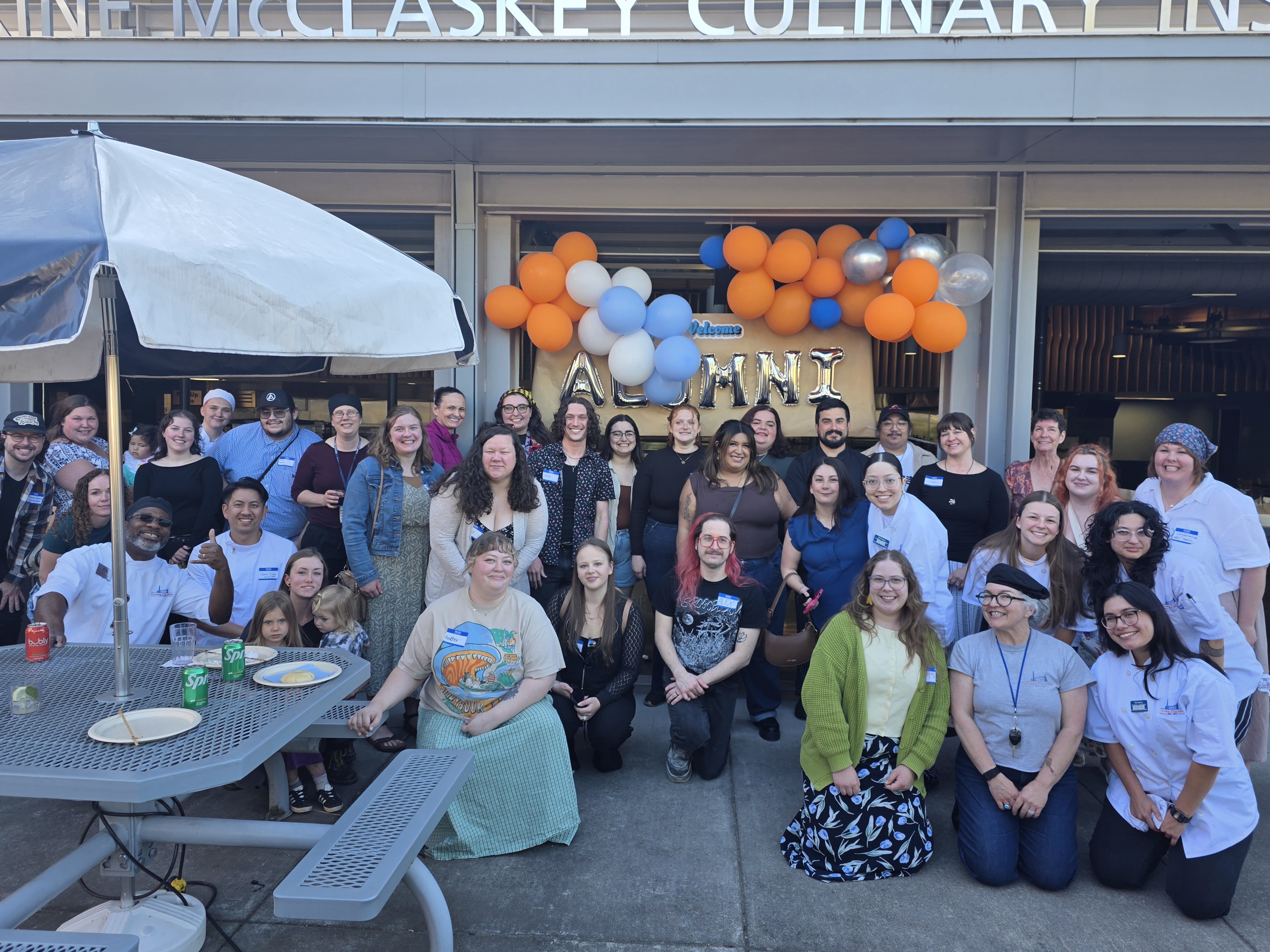 Clark Culinary students, alumni, and instructors gathered in front of the MCI, under a blue and orange balloon arch
