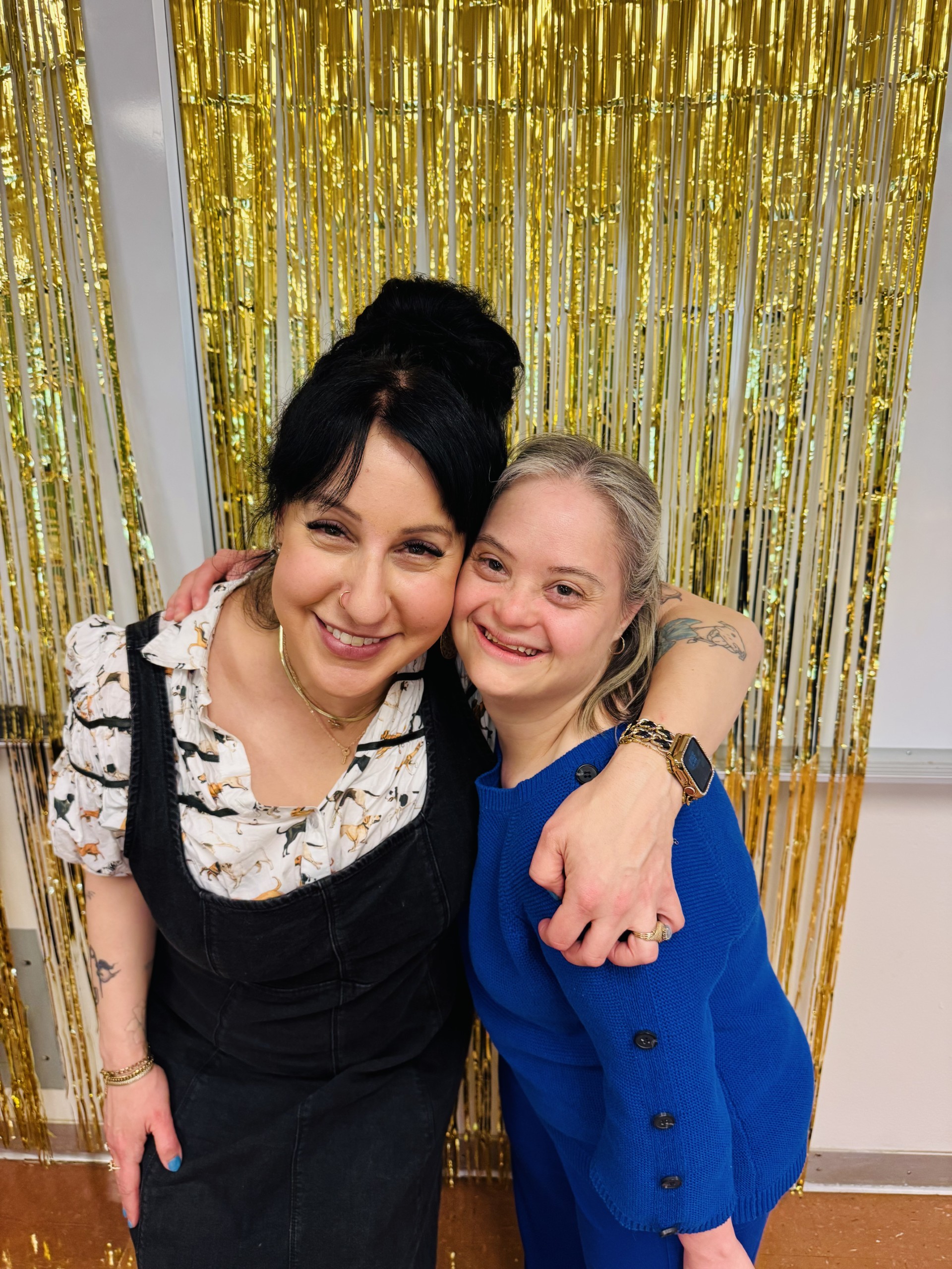 Niira and Vanessa smiling at the camera and hugging in front of a sparkly background