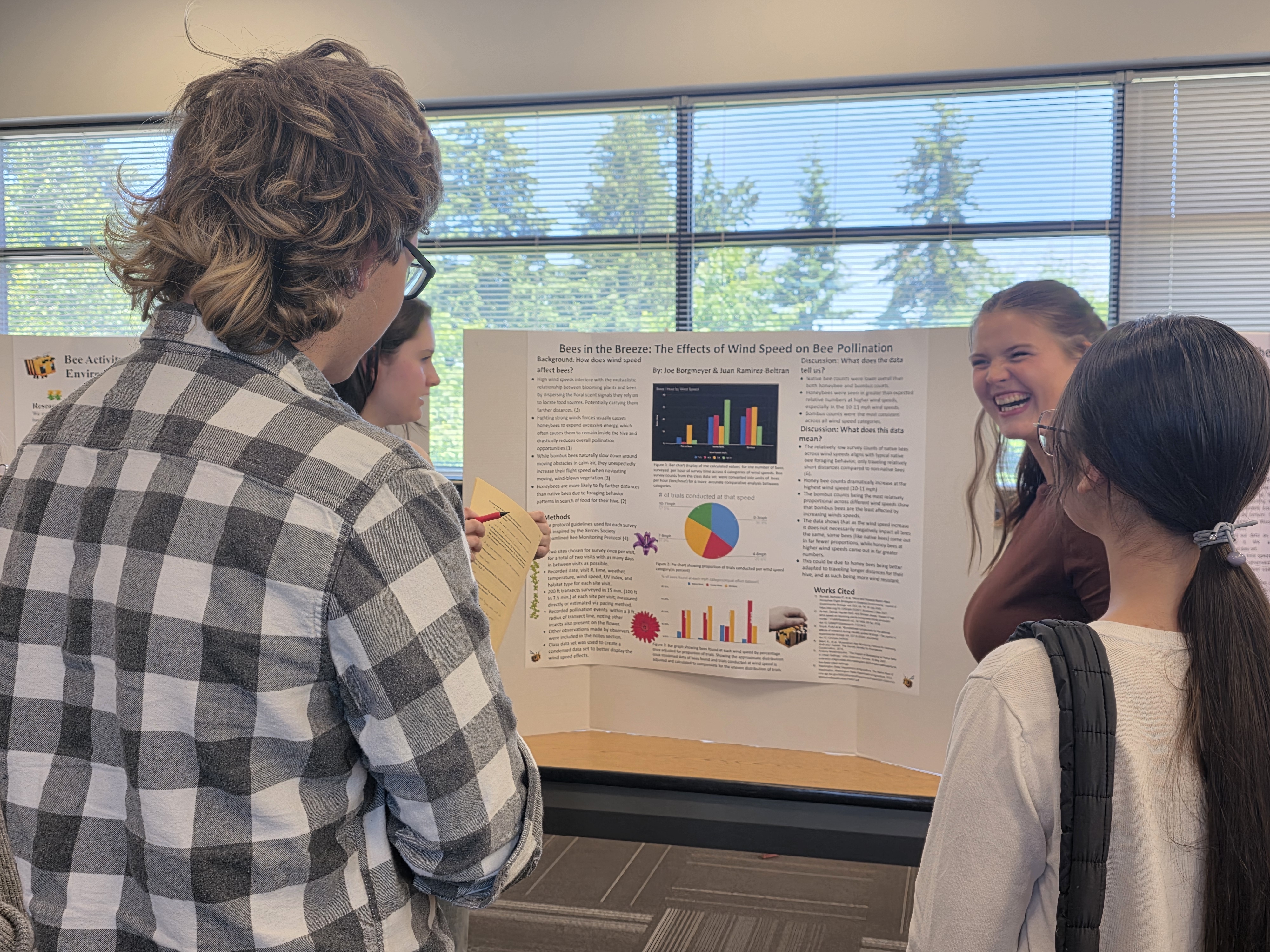 Biology student laughs while three event attendees look on at her poster while smiling