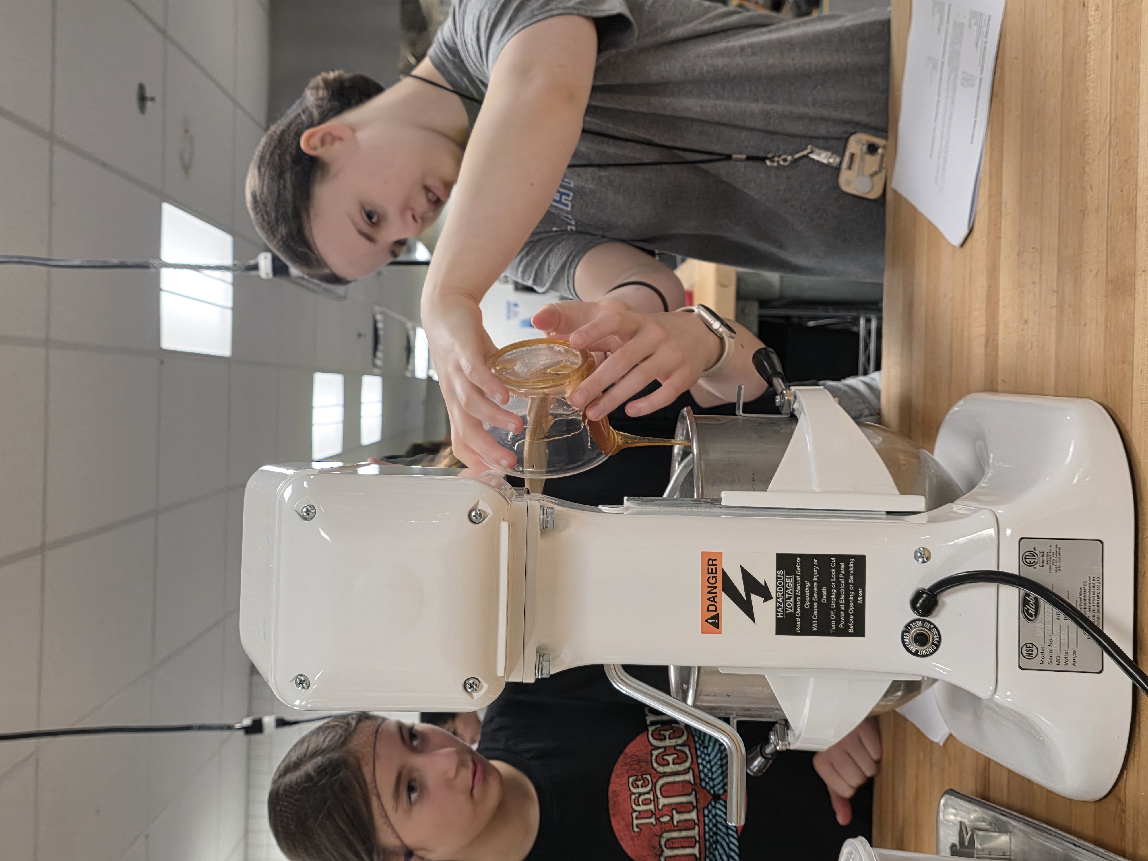 Students pour honey into a mixing bowl