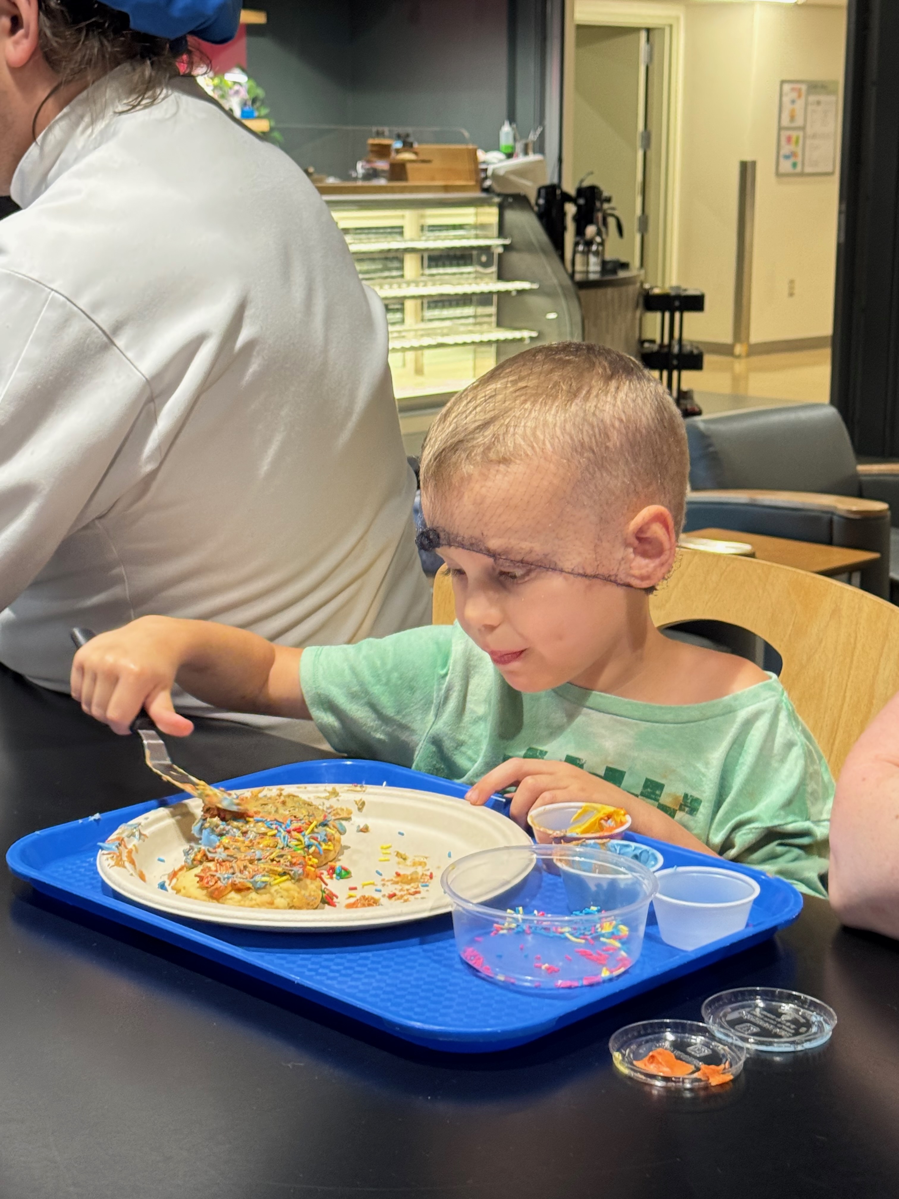 Little boy in a hairnet spreads frosting on a cookie