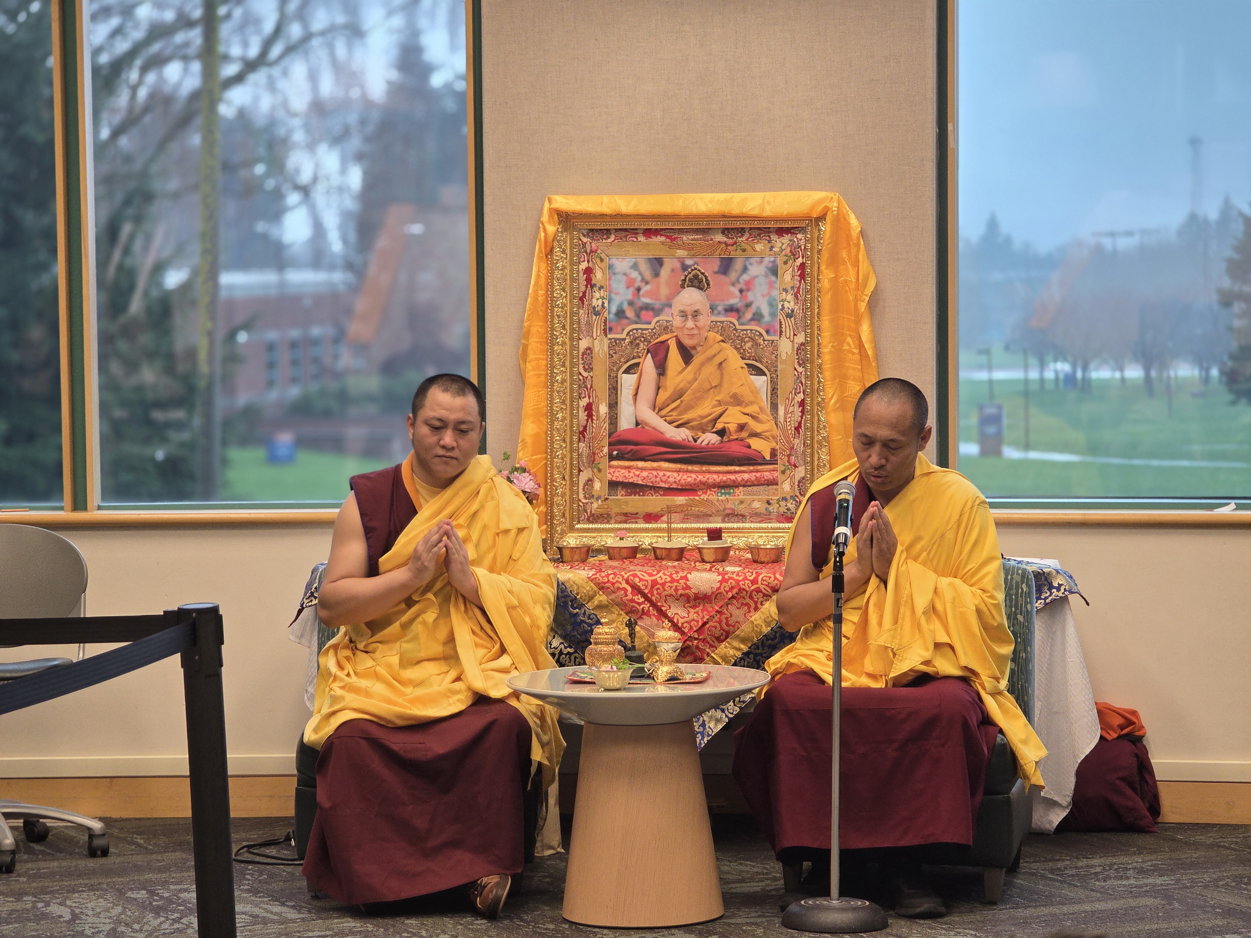 Two monks in maroon and yellow robes sitting in prayer