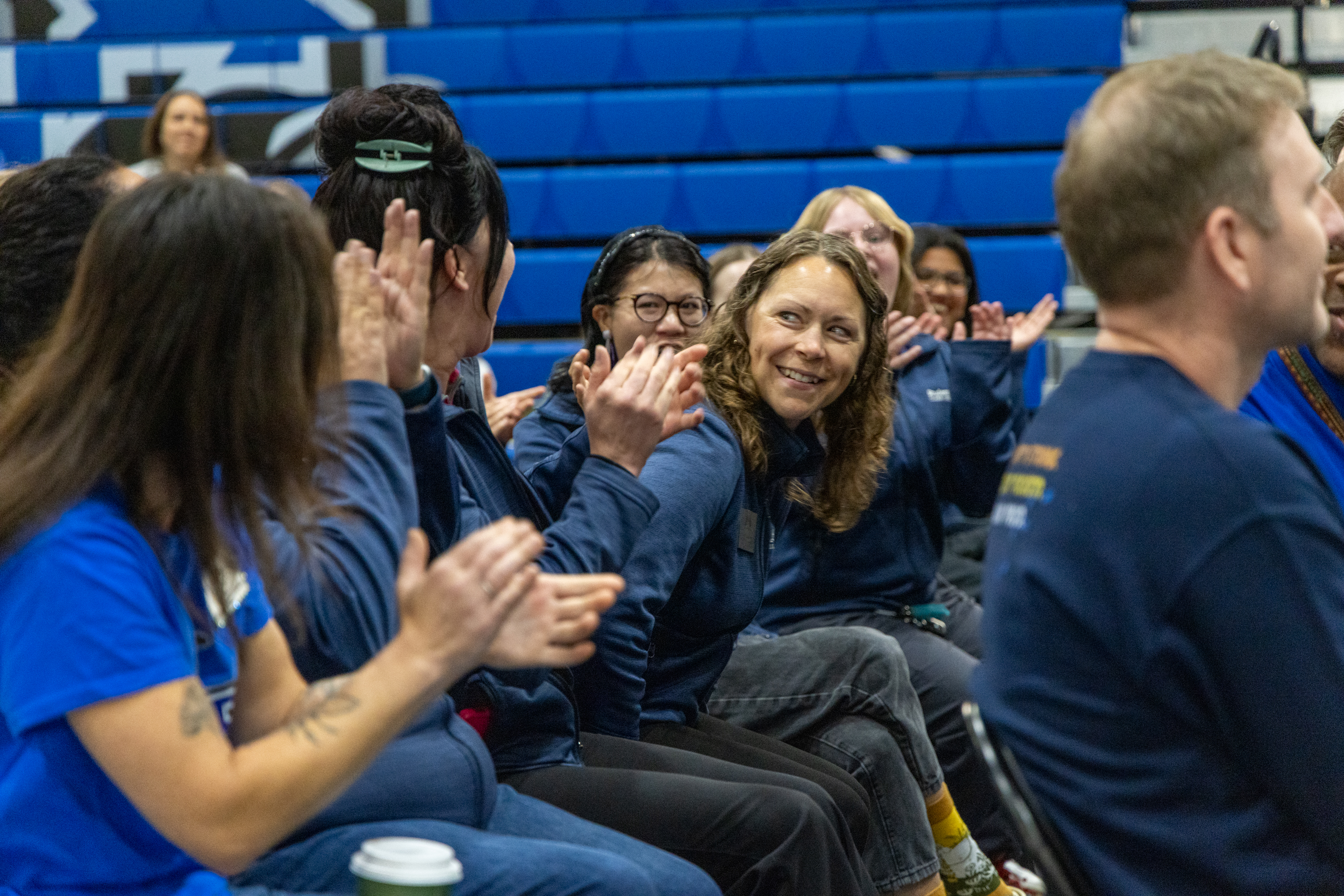 Employees sit in a row of chairs cheering as Sarah smiles while standing up