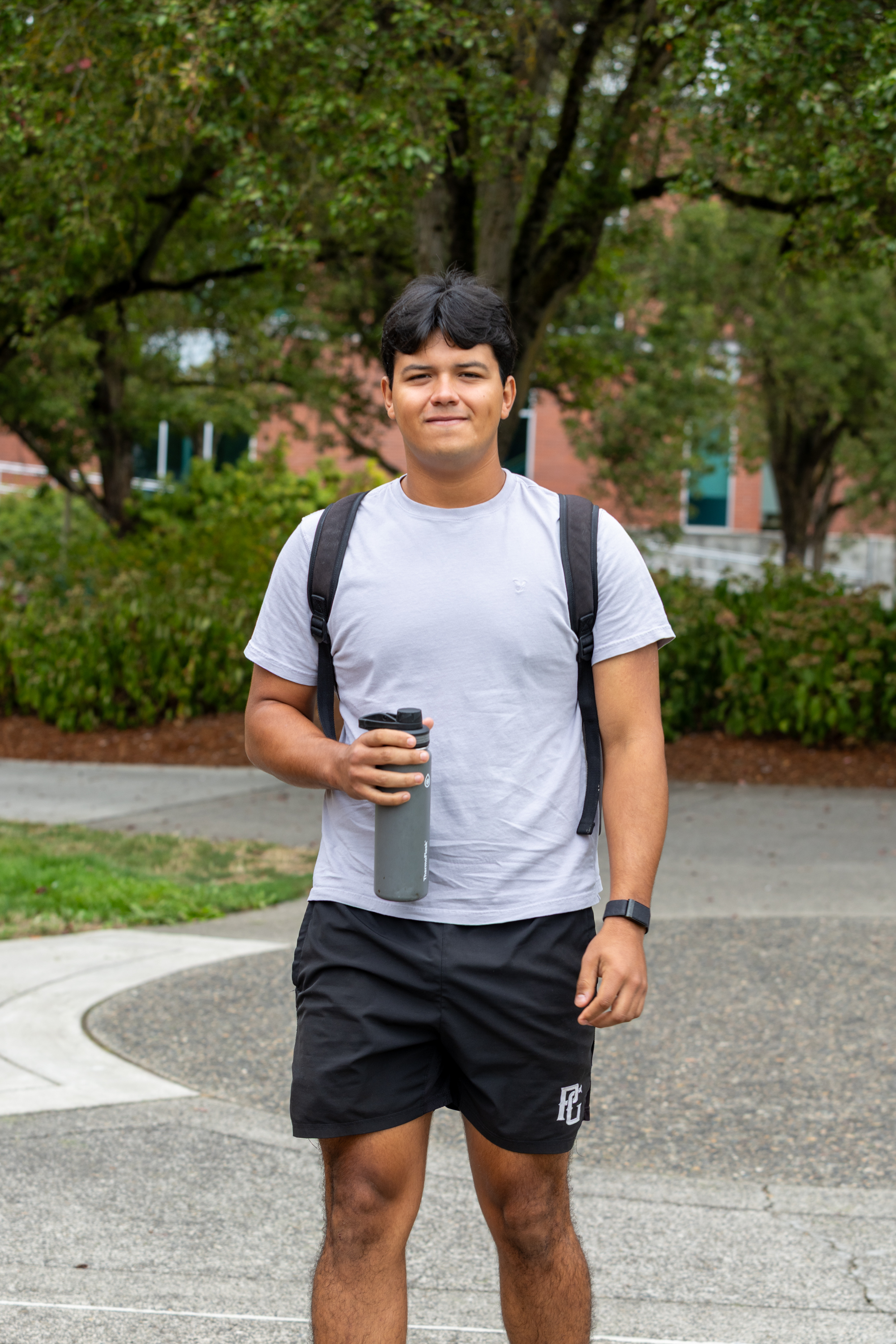 Student with backpack stands outside holding a coffee cup