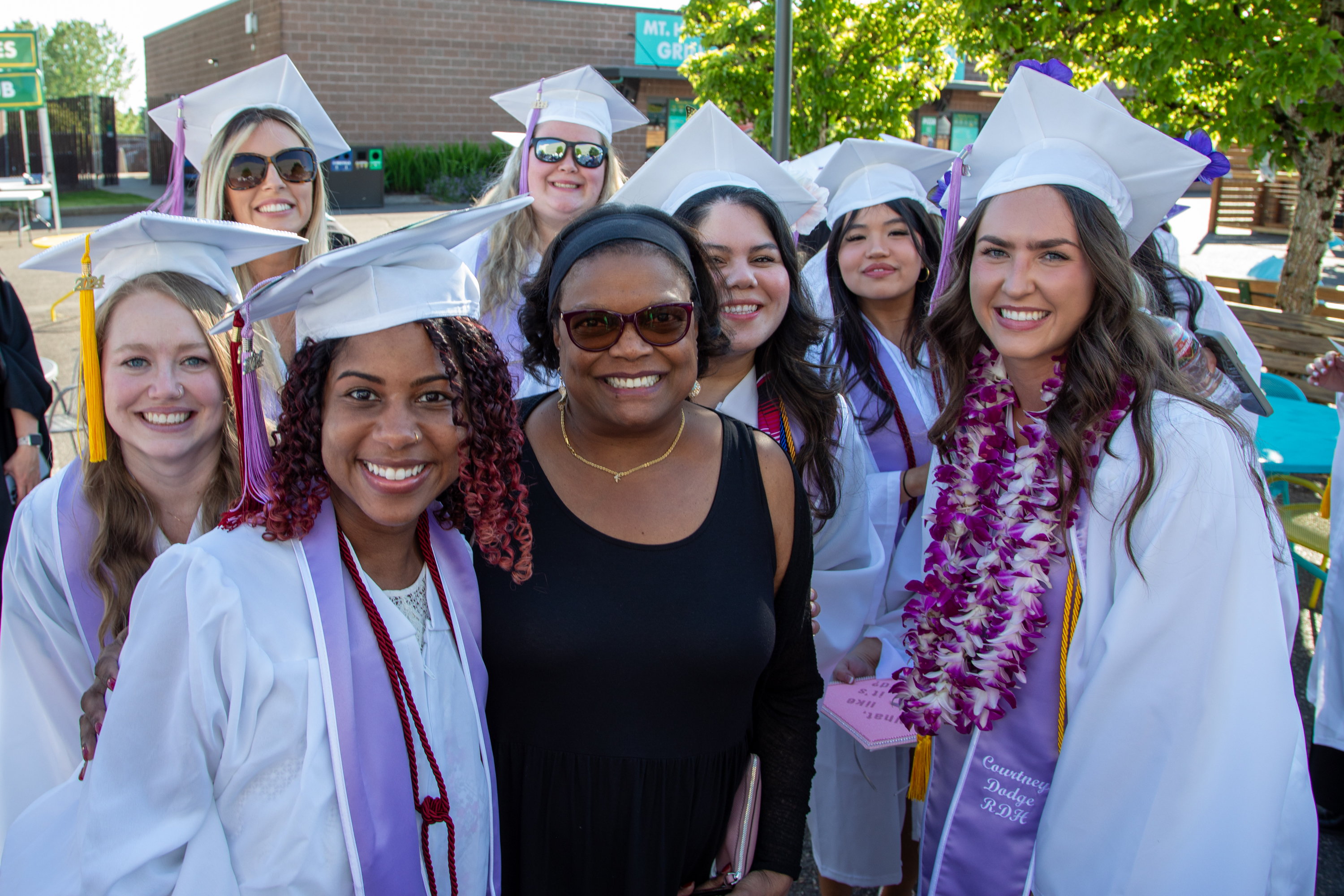Dr. Karin Edwards smiling in the middle of group of dental hygiene graduates in cap and gowns