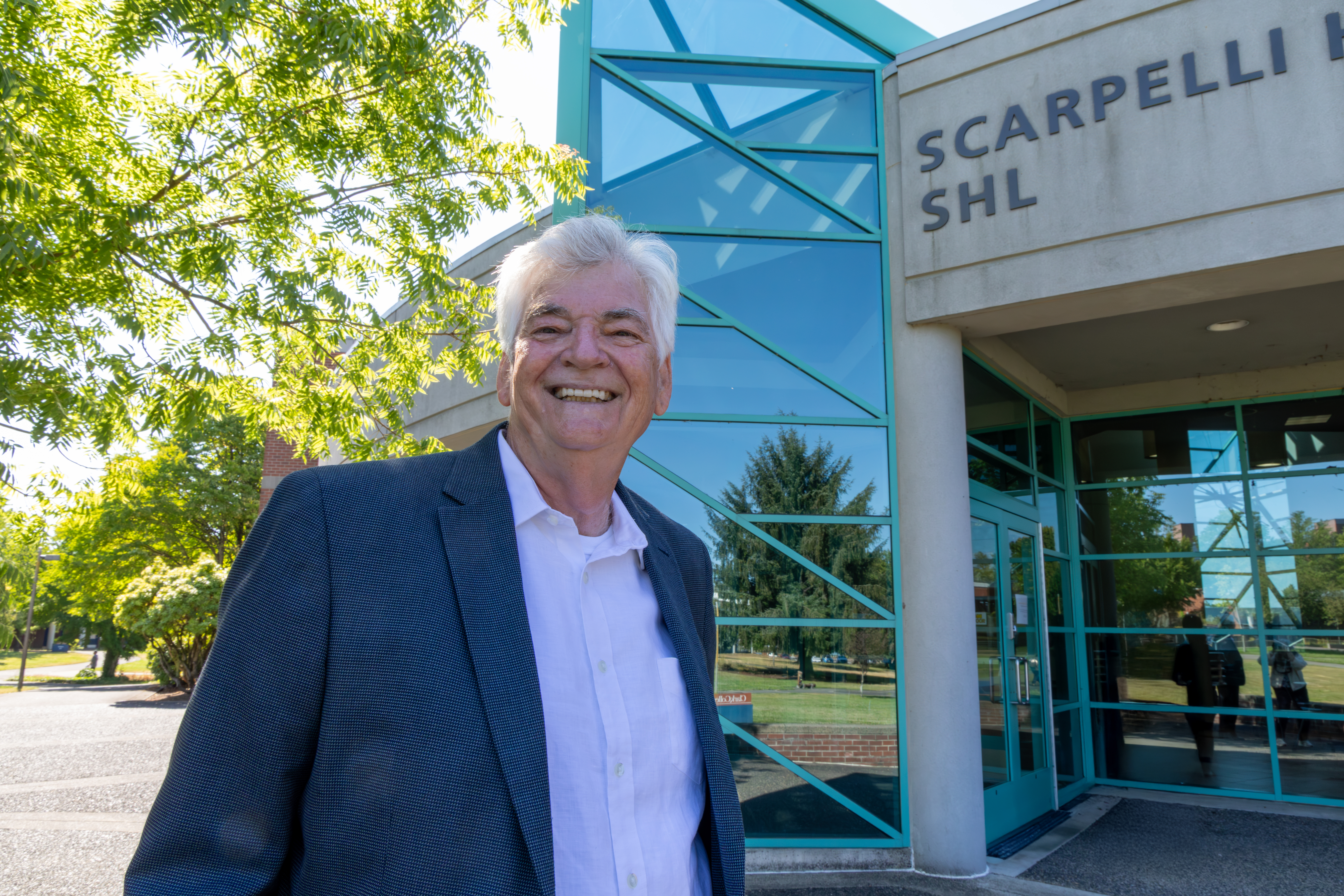 James Ron Powers stands smiling in front of Scarpelli Hall