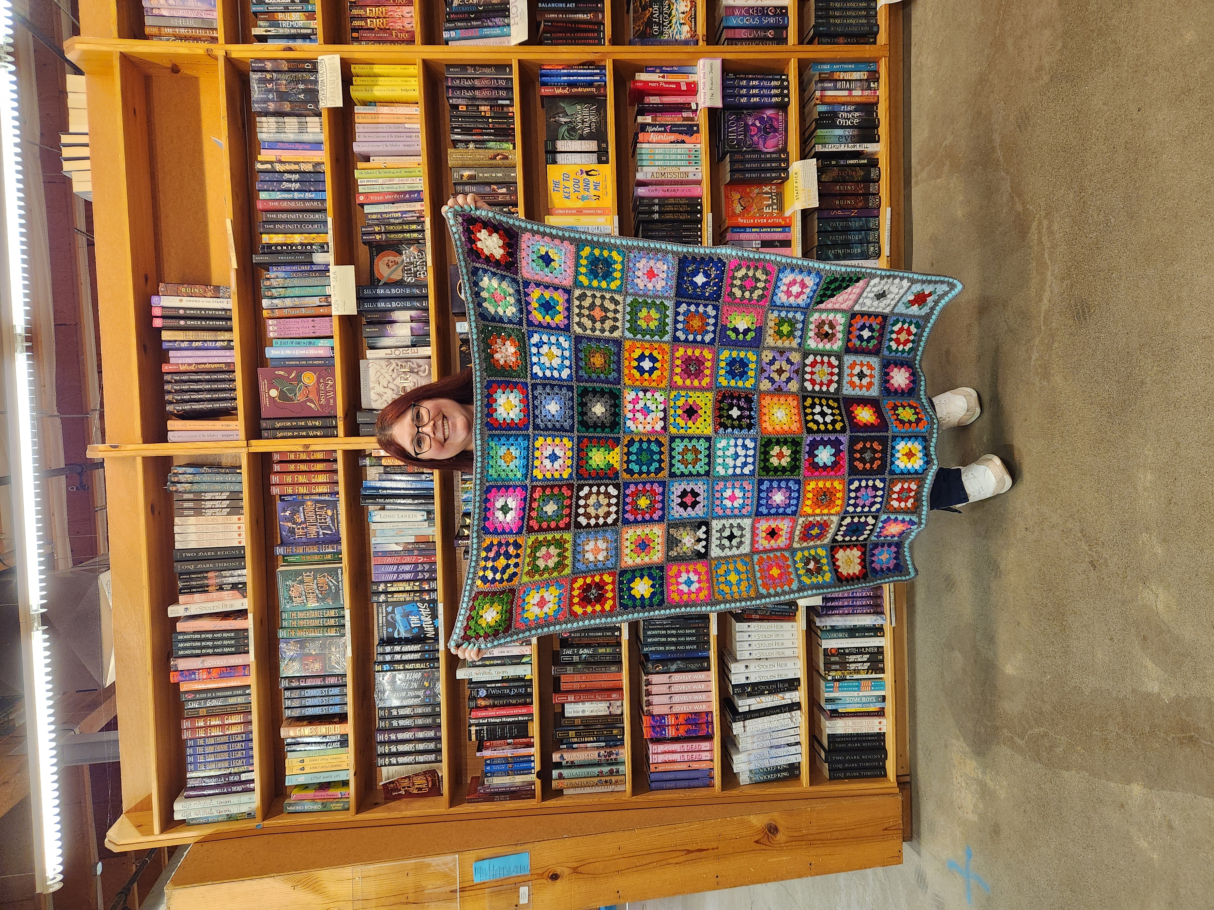 Laura holds up a crocheted blanket in front of shelves of books