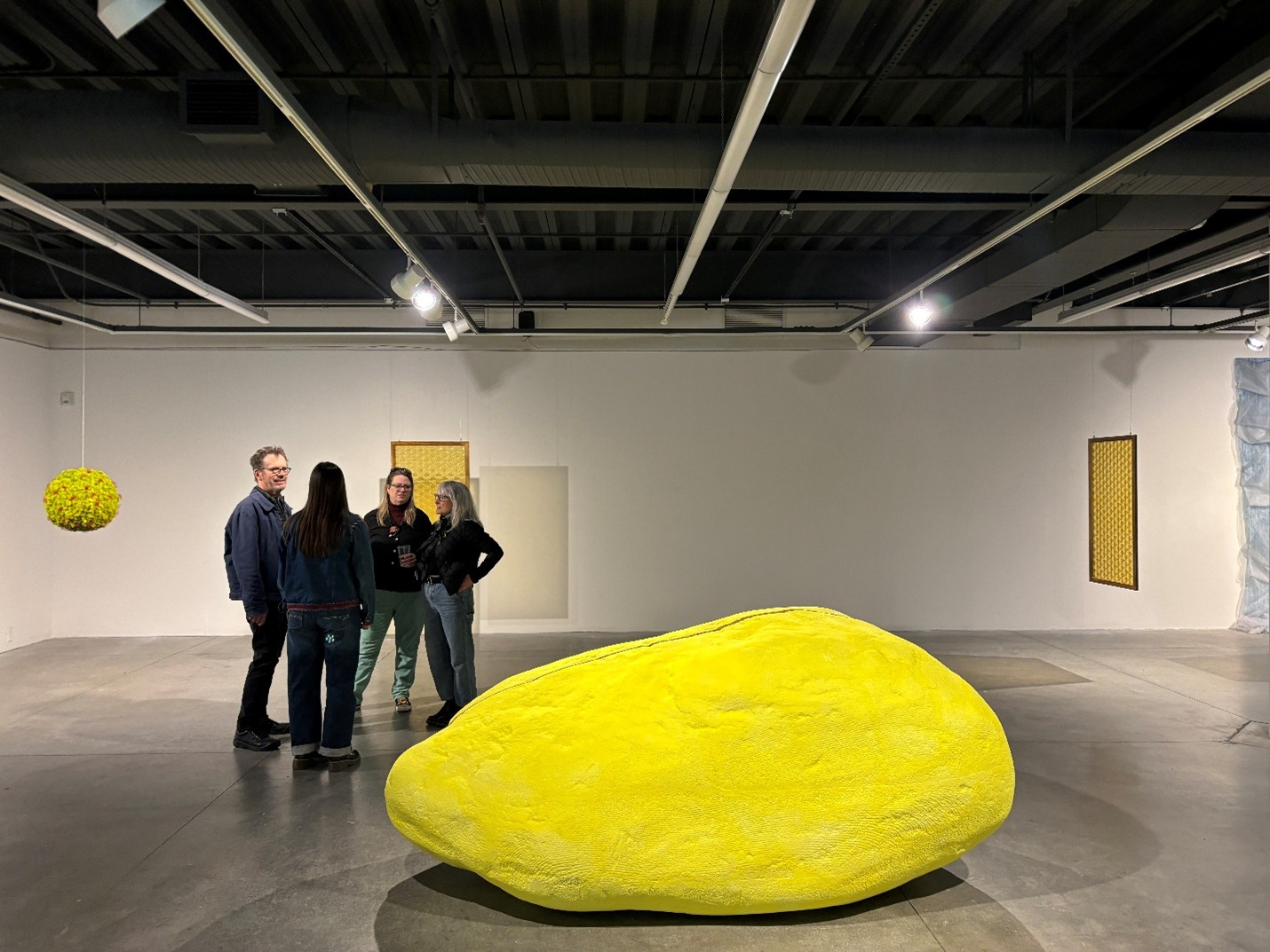 Artist Nan Curtis standing with art gallery visitors next to yellow rock sculpture