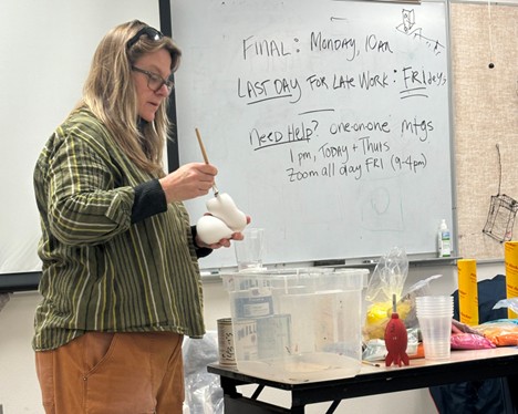 Nan Curtis stands in front of a classroom and applies glue to a plaster sculpture, preparing it for flocking.
