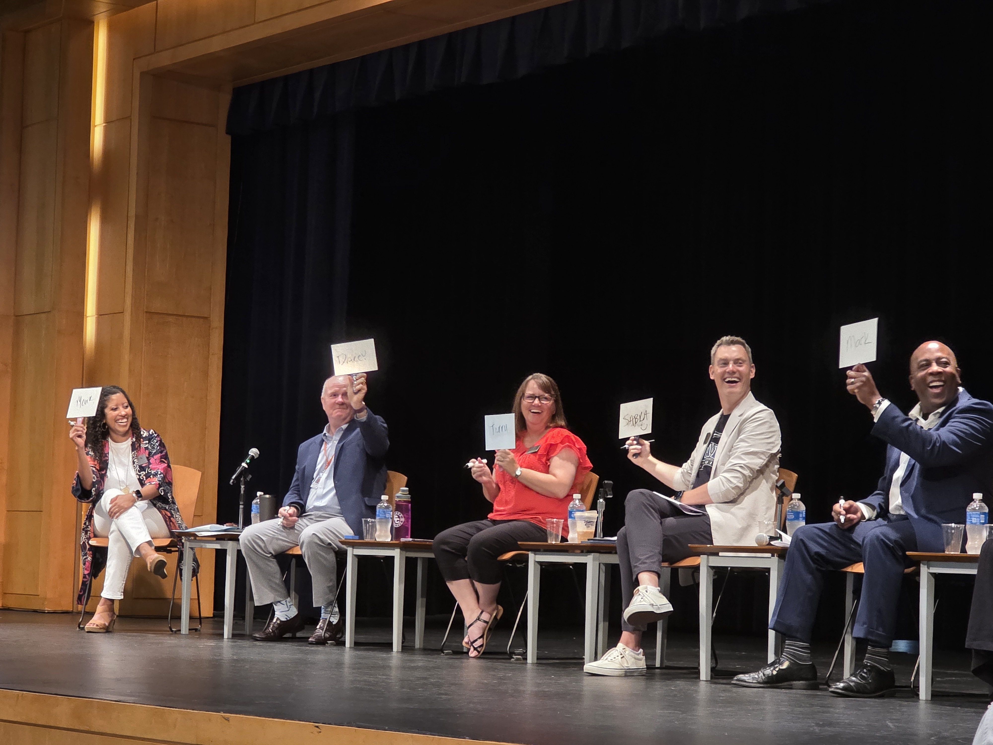 Panelists on stage holding up whiteboards and laughing