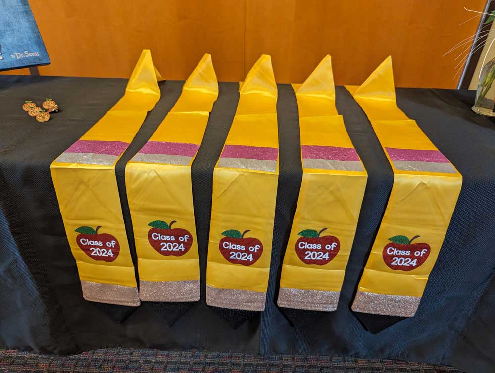 BASTE Class of 2024 graduation stoles displayed neatly, featuring an apple graphic with the text 'Class of 2024' on it.