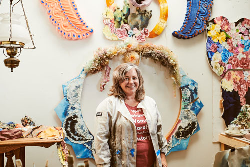 A smiling person in the foreground with a backdrop of various artworks.