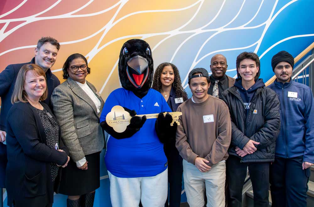 A group of people pose for a picture, with a penguin mascot in the center holding a large key.