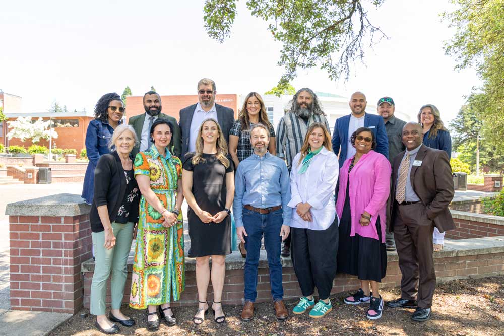 A group of tenured professors smiling and posing for a photo on a sunny college campus.